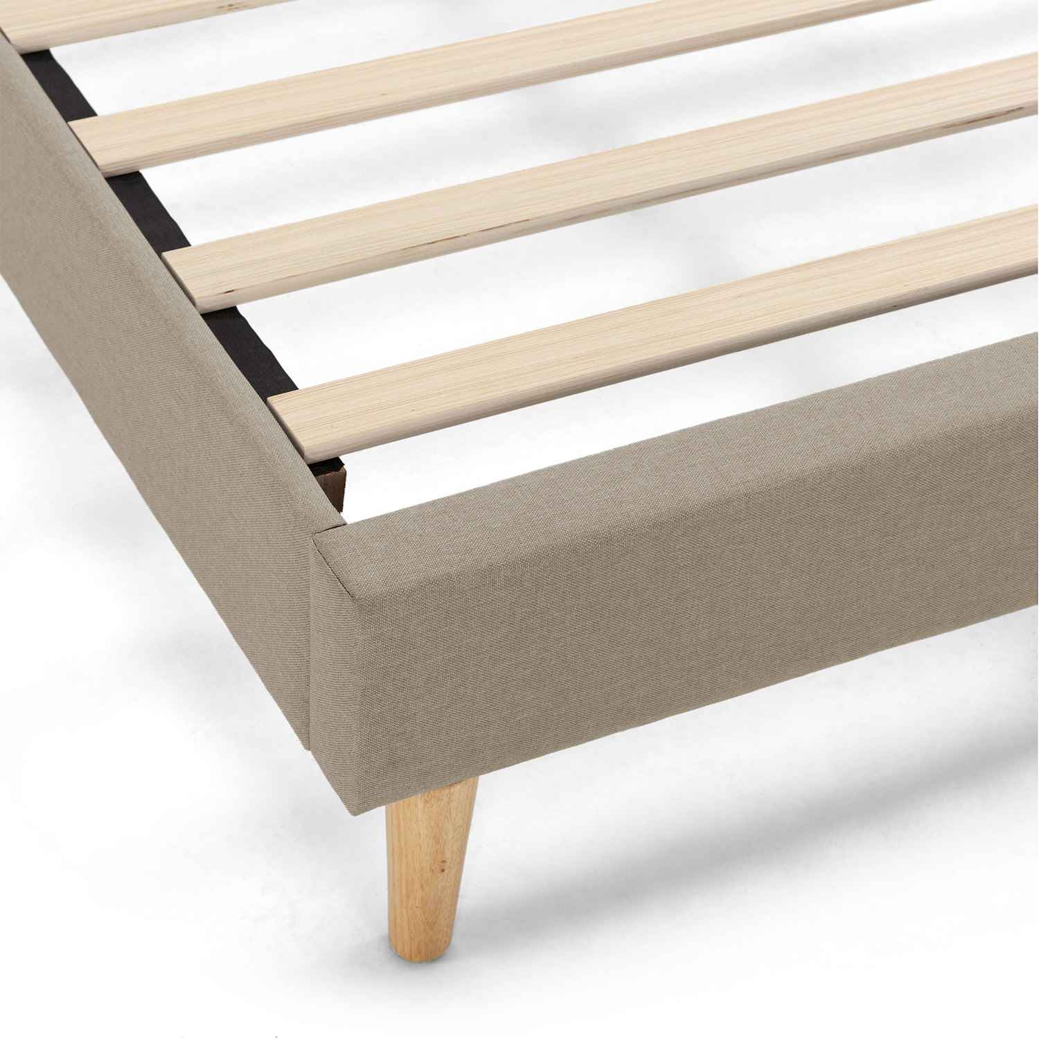 Primer plano de un somier tapizado en beige con listones de madera y una pata inclinada.