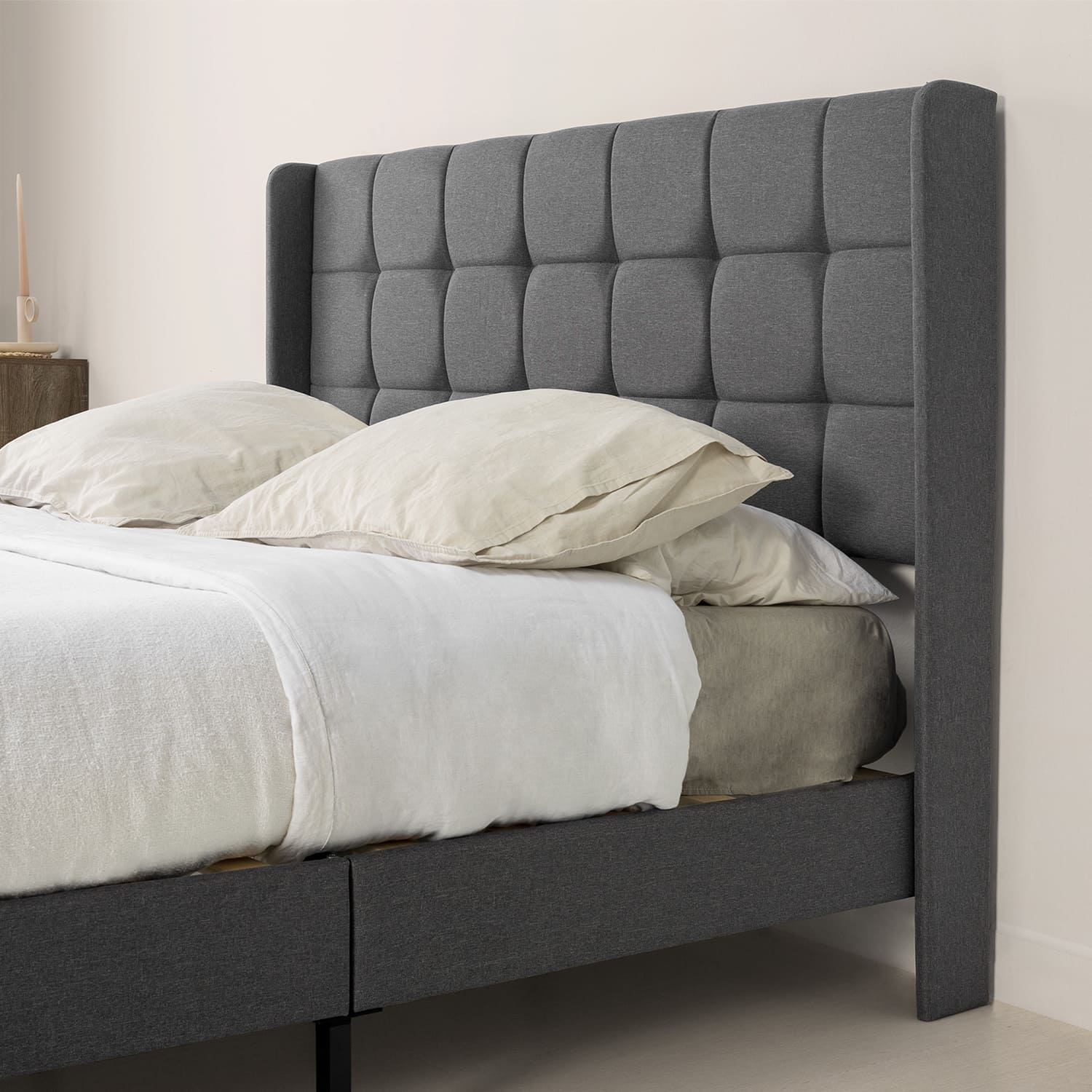 Una cama gris con cabecero tapizado, almohadas blancas y beige visibles.