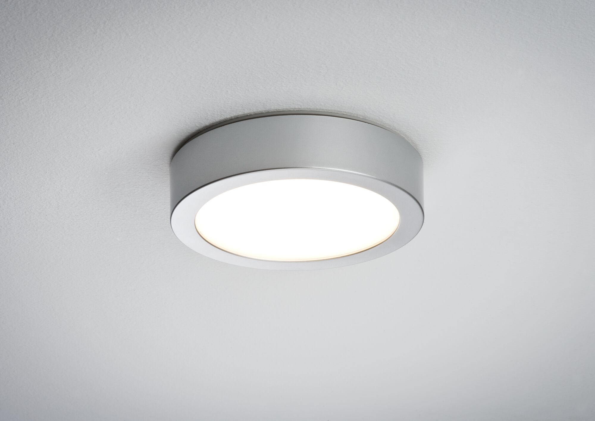 Una plafoniera rotonda argentata che emette luce brillante su sfondo bianco.