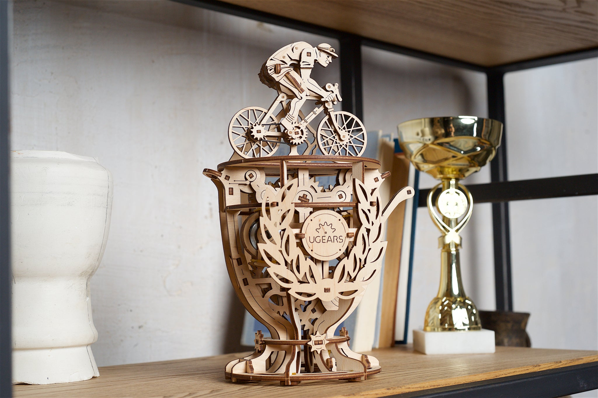 Drewniany model kolarza na trofeum, z białym wazonem i złotym pucharem.