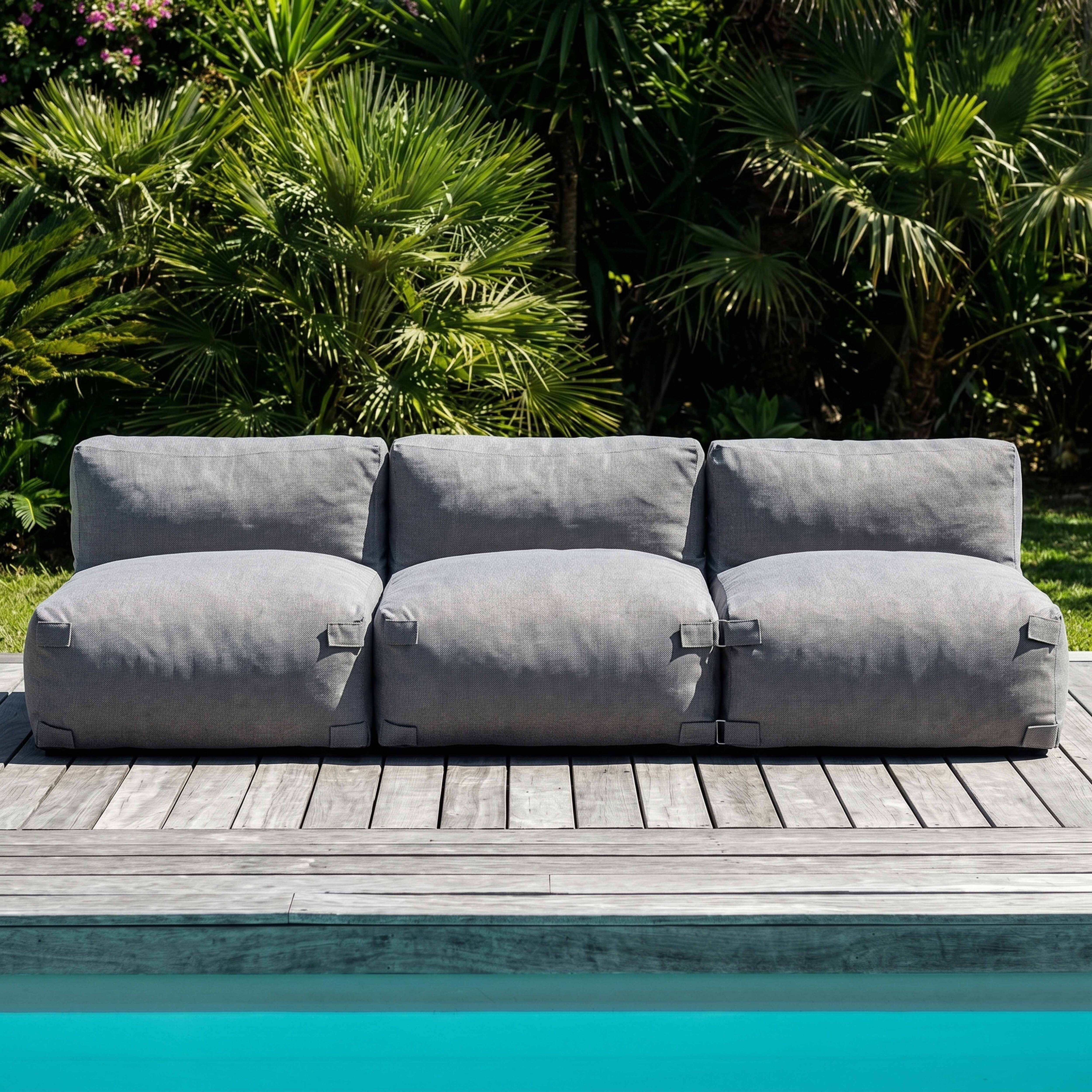 Ein graues Outdoor-Sofa steht auf einer Holzterrasse neben einem Pool.