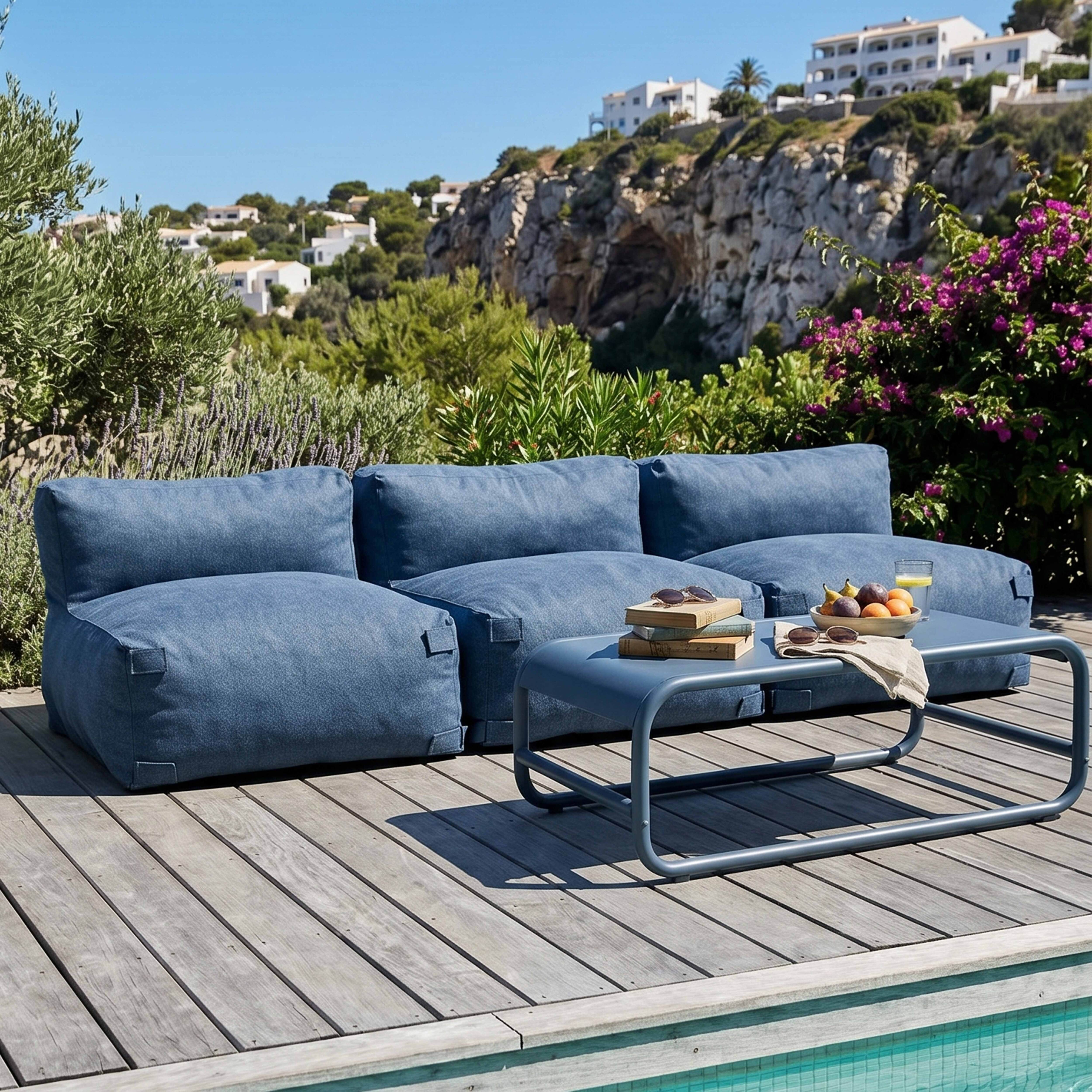 Ein blaues Outdoor-Sofa und ein Tisch mit Früchten und Büchern auf einer Holzterrasse.
