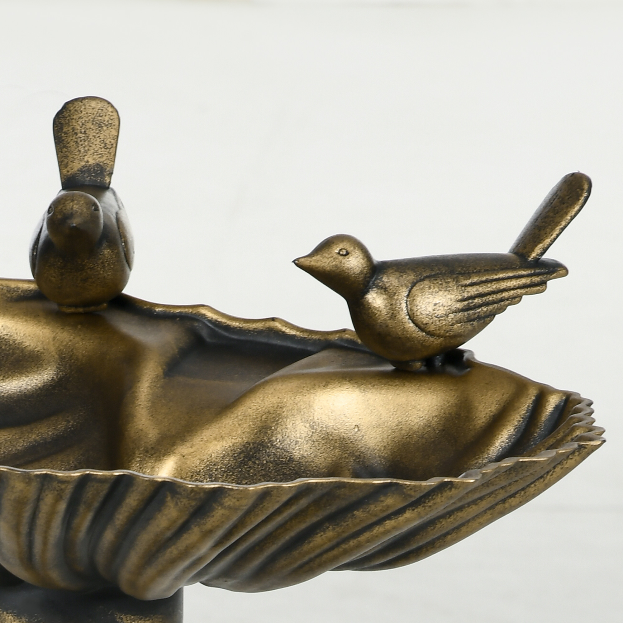 Pajarera de bronce con dos pájaros sobre base de concha, fondo claro.