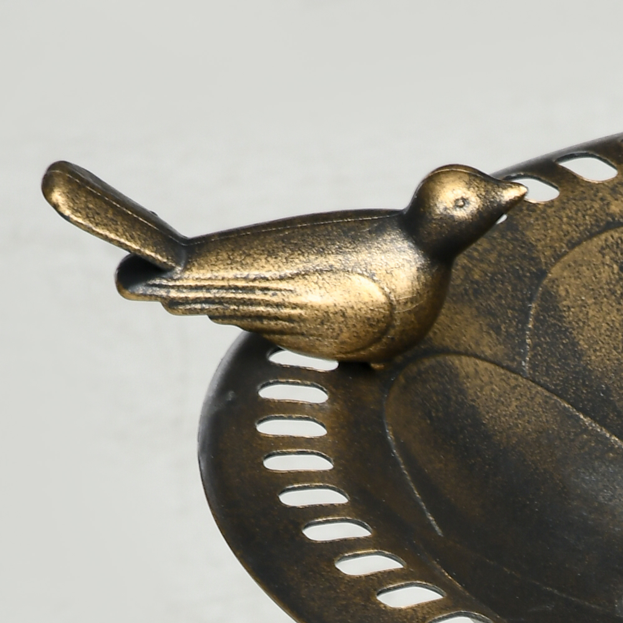 Una figura de pájaro de bronce se posa sobre un plato decorativo de metal con recortes.