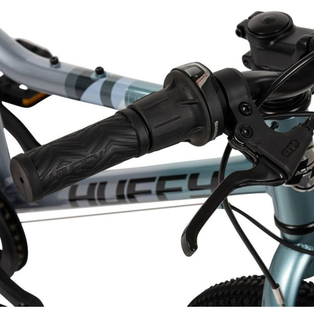 Nahaufnahme eines Fahrradlenkers mit schwarzem Griff und Gangschaltung. Blauer Rahmen mit Streifen.