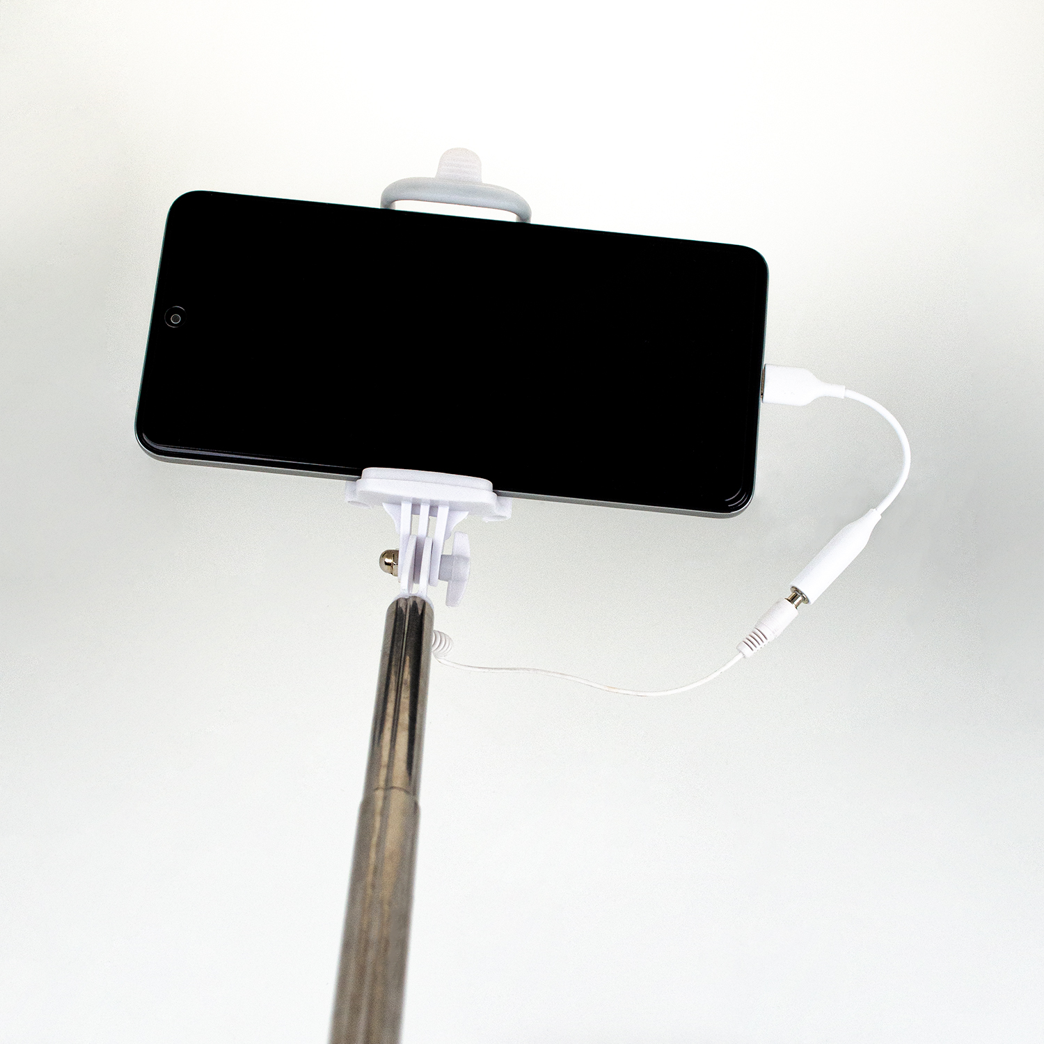 Bir akıllı telefon selfie çubuğuna takılı ve beyaz bir kabloyla bağlı.