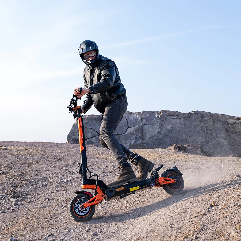 Mann in Lederjacke fährt Roller im Gelände, Staub wirbelt auf.