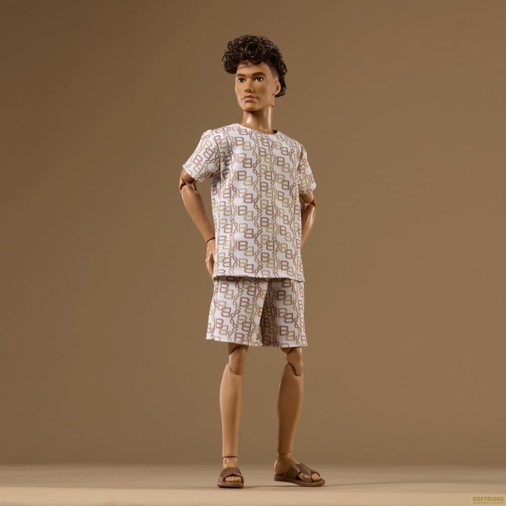 Männliche Puppe mit lockigem Haar trägt ein weißes Shirt und Shorts mit braunem Muster.