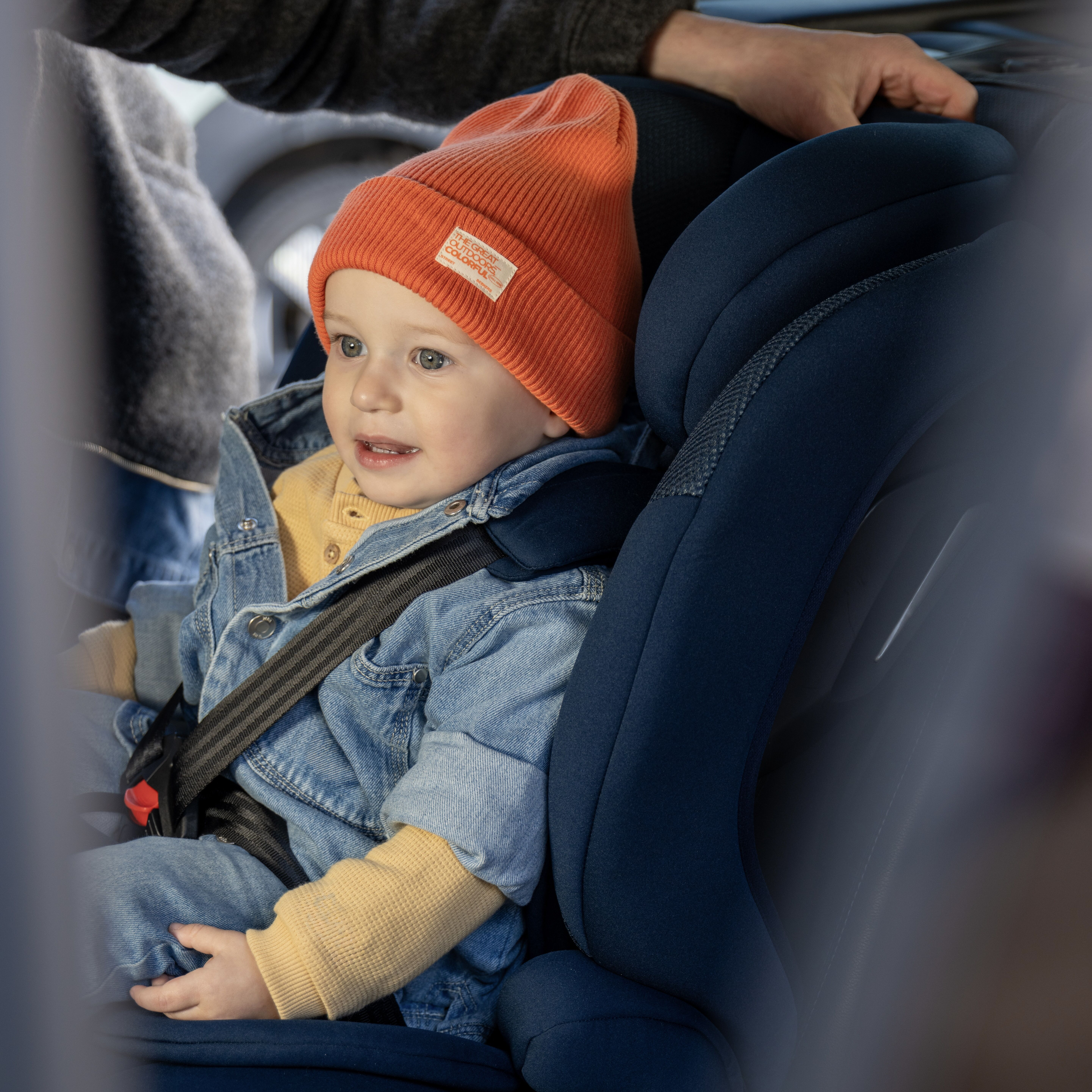 Ein Kleinkind mit Mütze sitzt in einem Autositz, angeschnallt.
