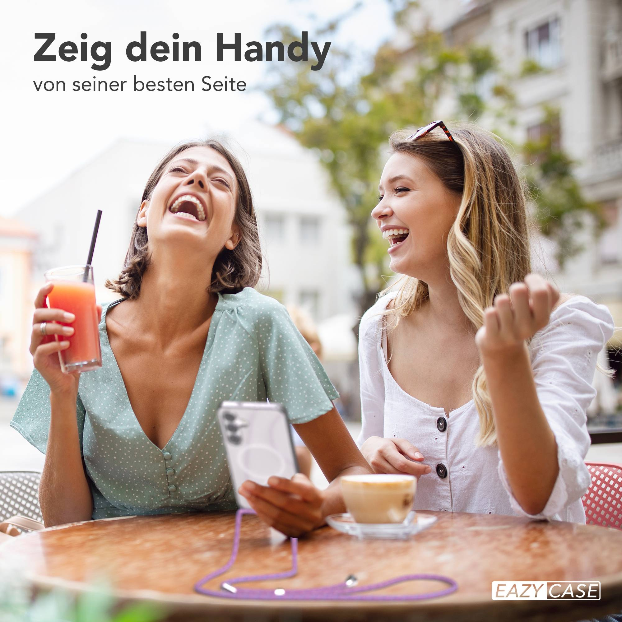 Zwei lachende Frauen sitzen an einem Tisch mit Getränken und einem Handy.