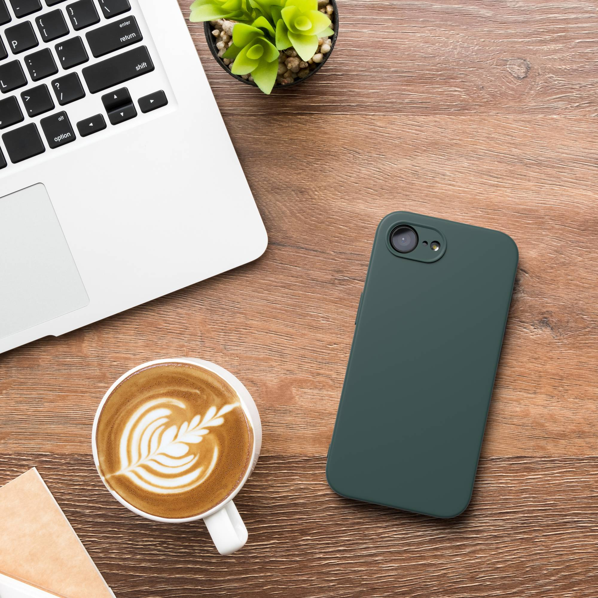 Ein Laptop, ein Handycase, ein Kaffee und eine Pflanze auf einem Holztisch.