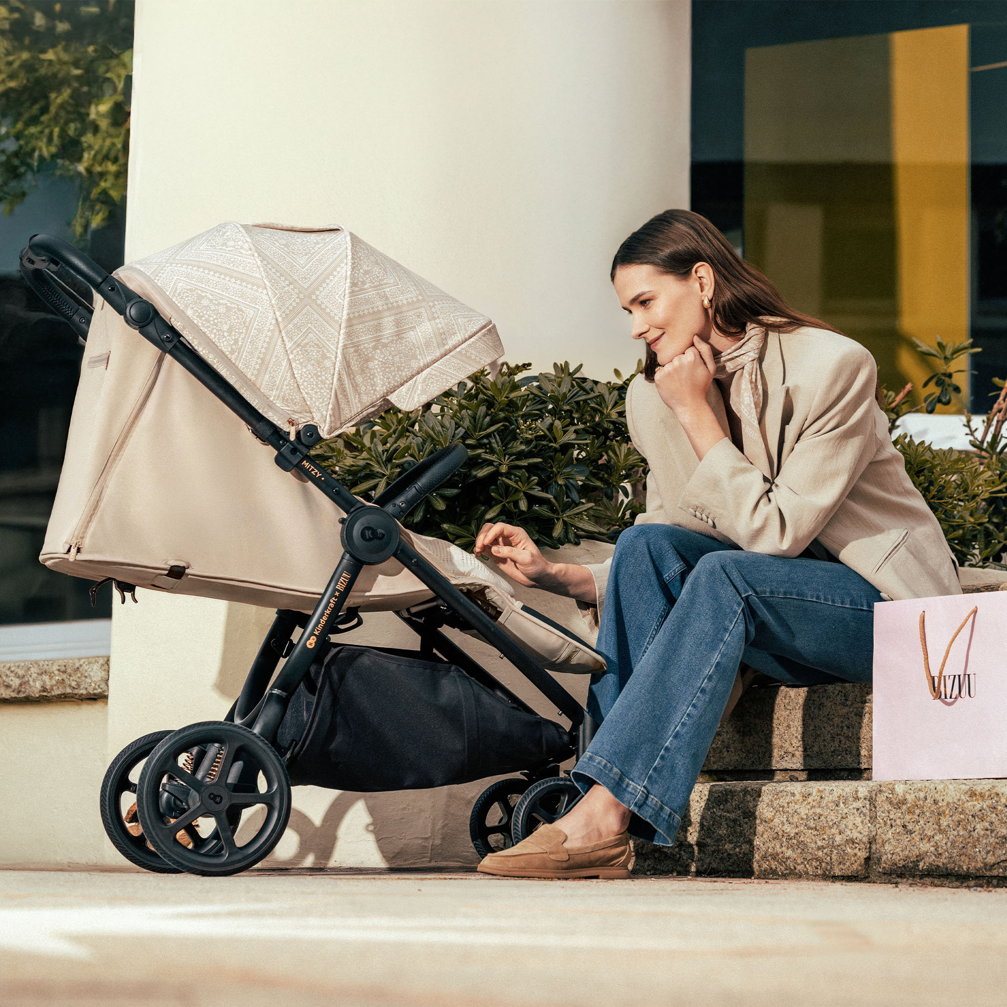 Eine Frau sitzt auf Stufen neben einem Kinderwagen, mit einer Einkaufstasche daneben.