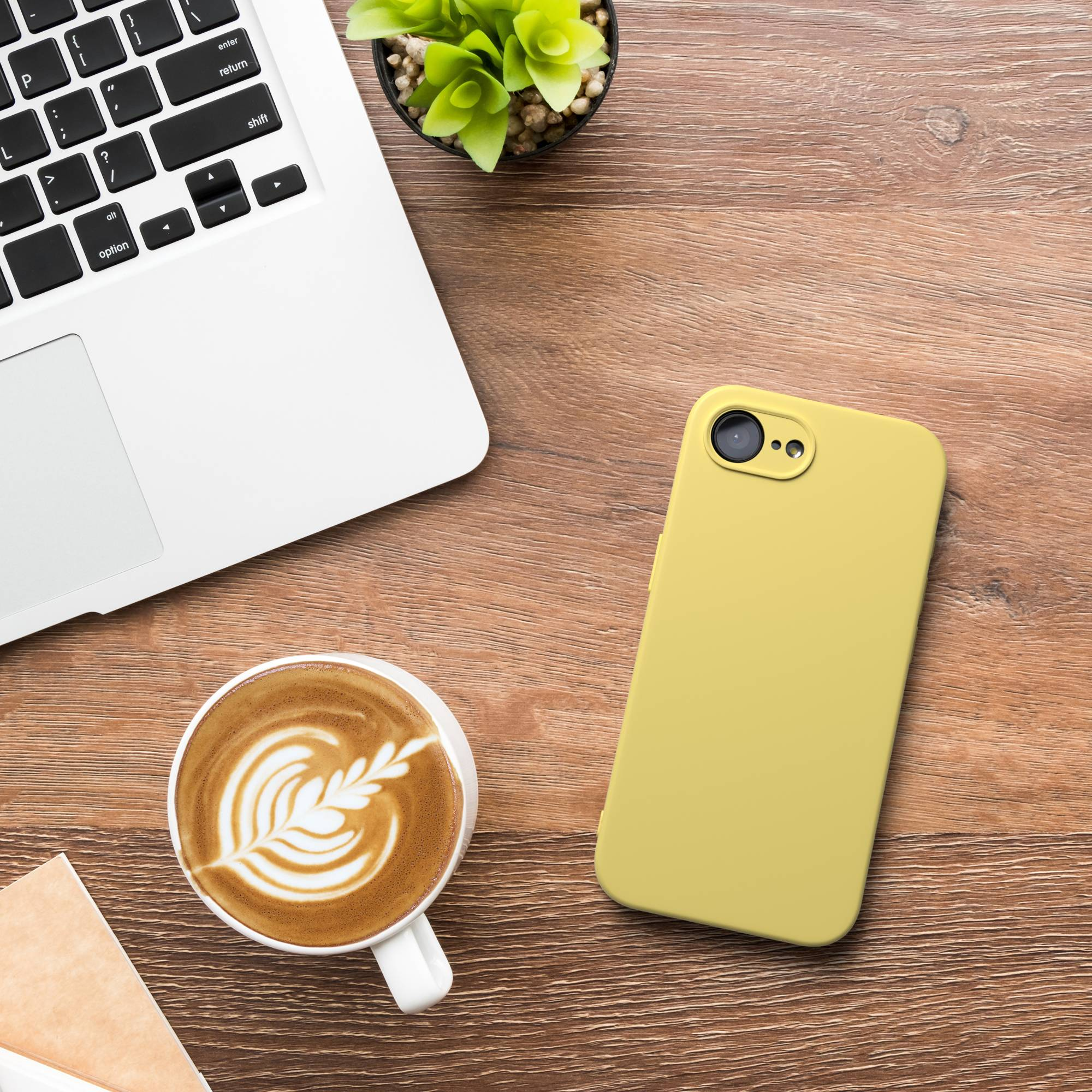 Ein Laptop, gelbe Handyhülle und Kaffee mit Latte Art auf Holztisch.