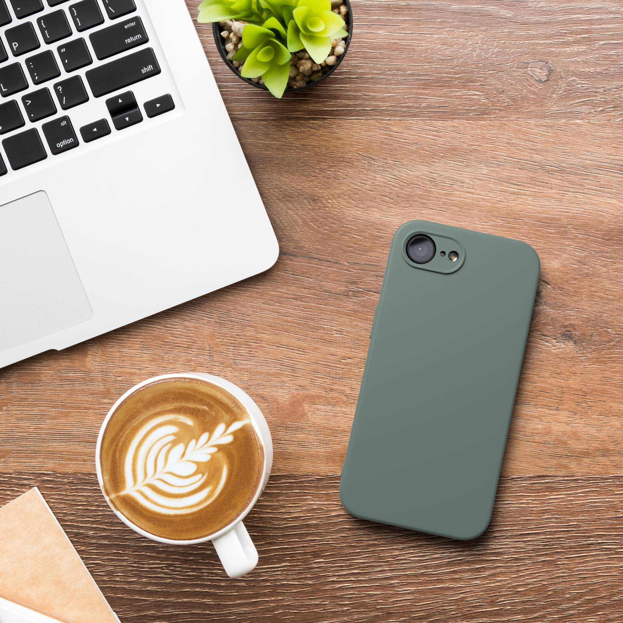 Ein Laptop, eine Kaffeetasse mit Latte Art und ein Handy liegen auf einem Holztisch.