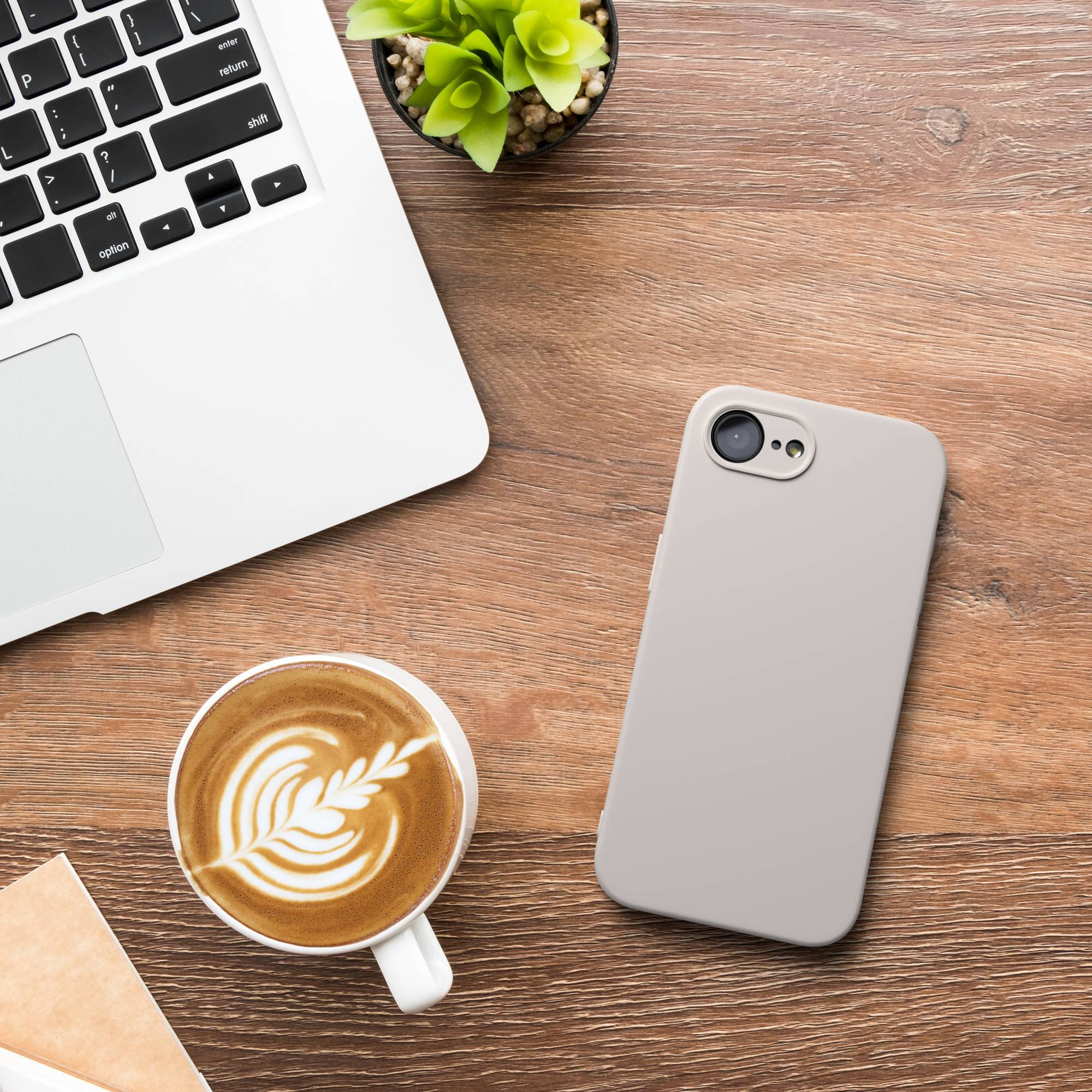 Ein Laptop, ein Handy und ein Kaffee mit Latte Art stehen auf einem Holztisch. Eine Topfpflanze ist in der Nähe des Laptops.