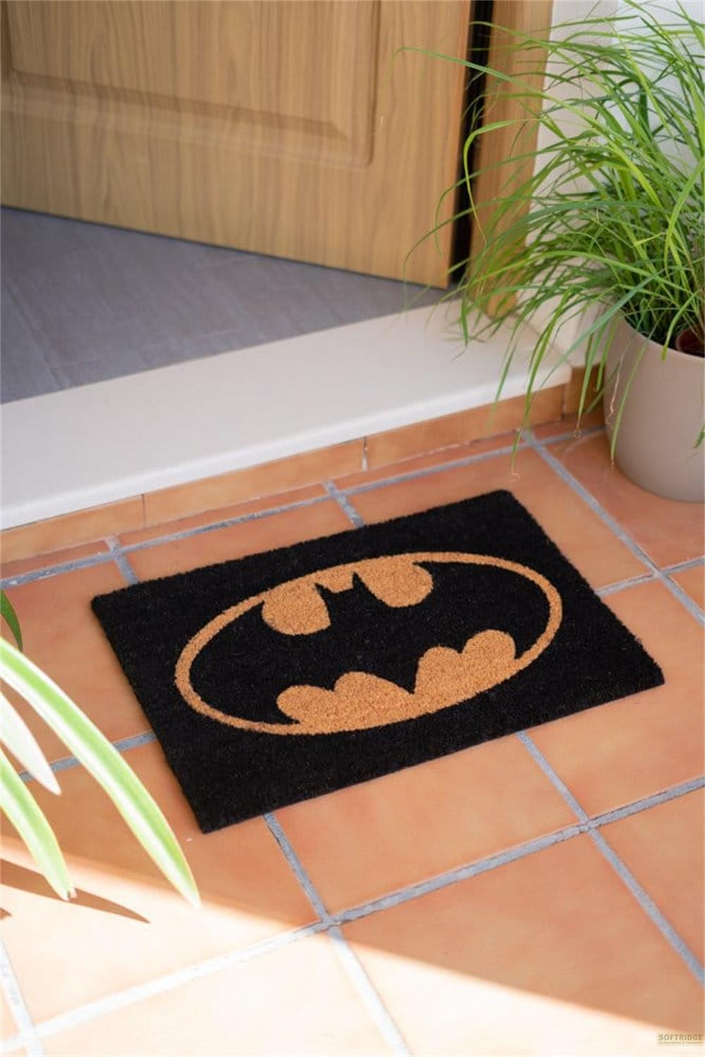 Schwarze Fußmatte mit Batman-Logo auf terrakottafarbenen Fliesen.