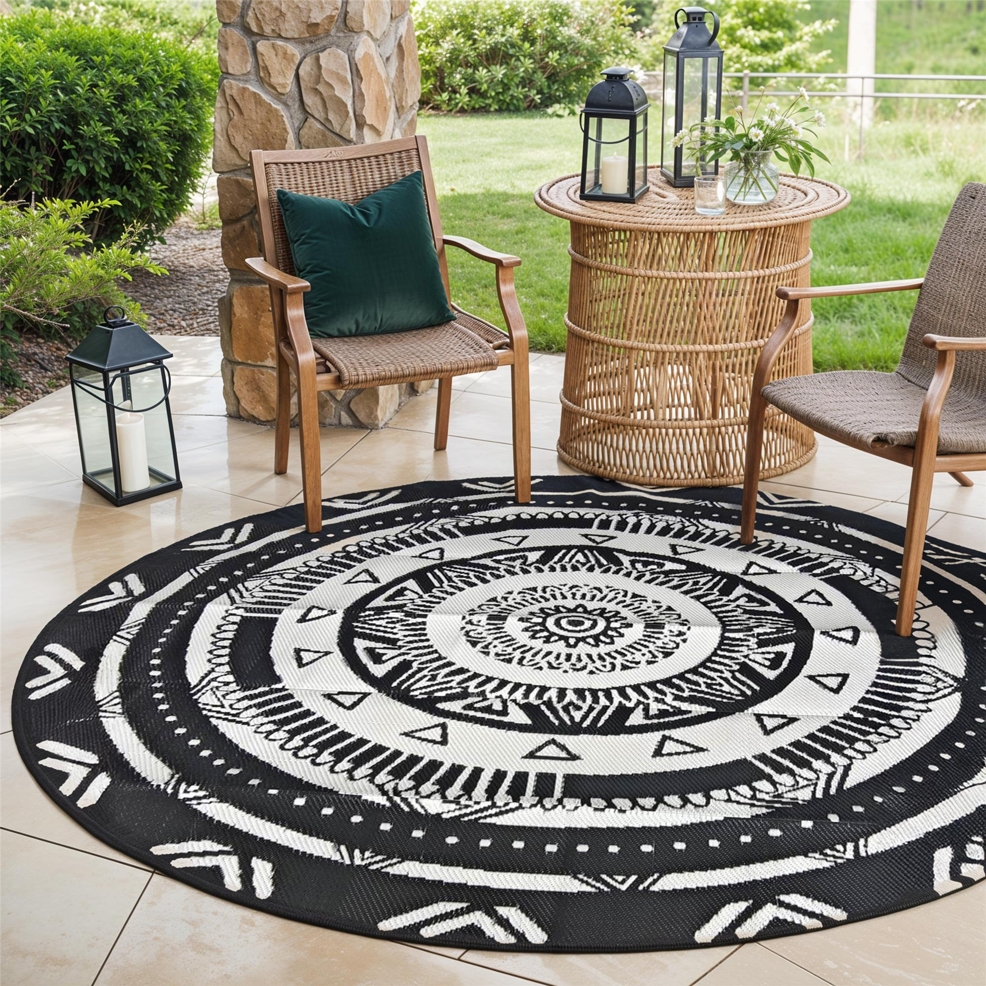 Runde schwarz-weiße Ethno-Teppich auf einer Terrasse mit zwei Korbstühlen und Laternen.