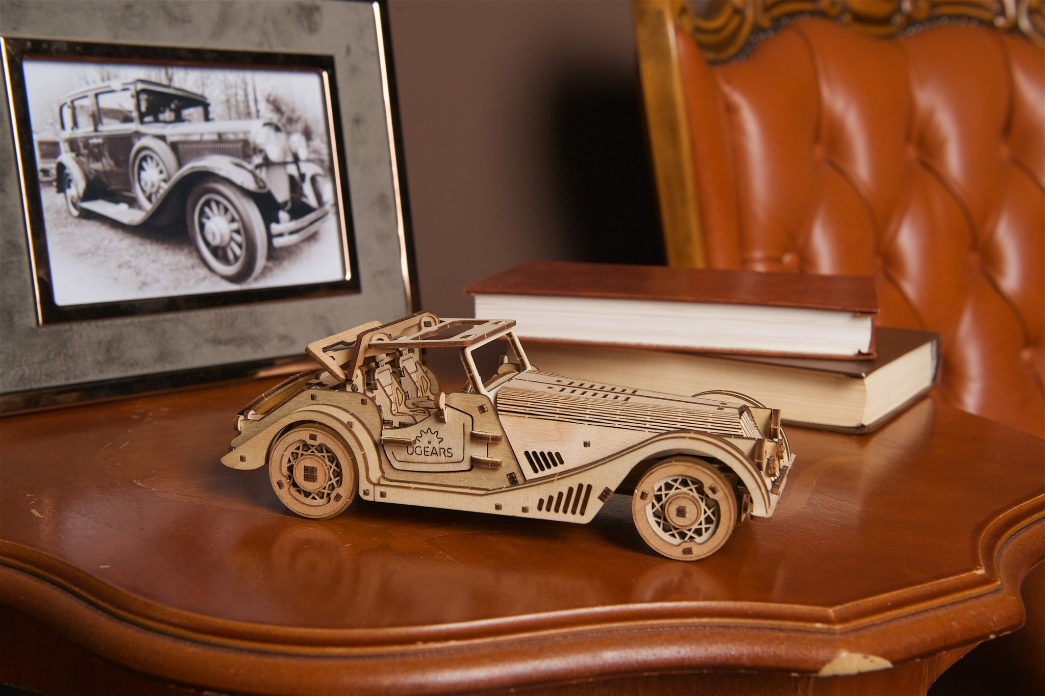 Modellino auto in legno su tavolo con foto incorniciata e libri. Sedia in pelle dietro.