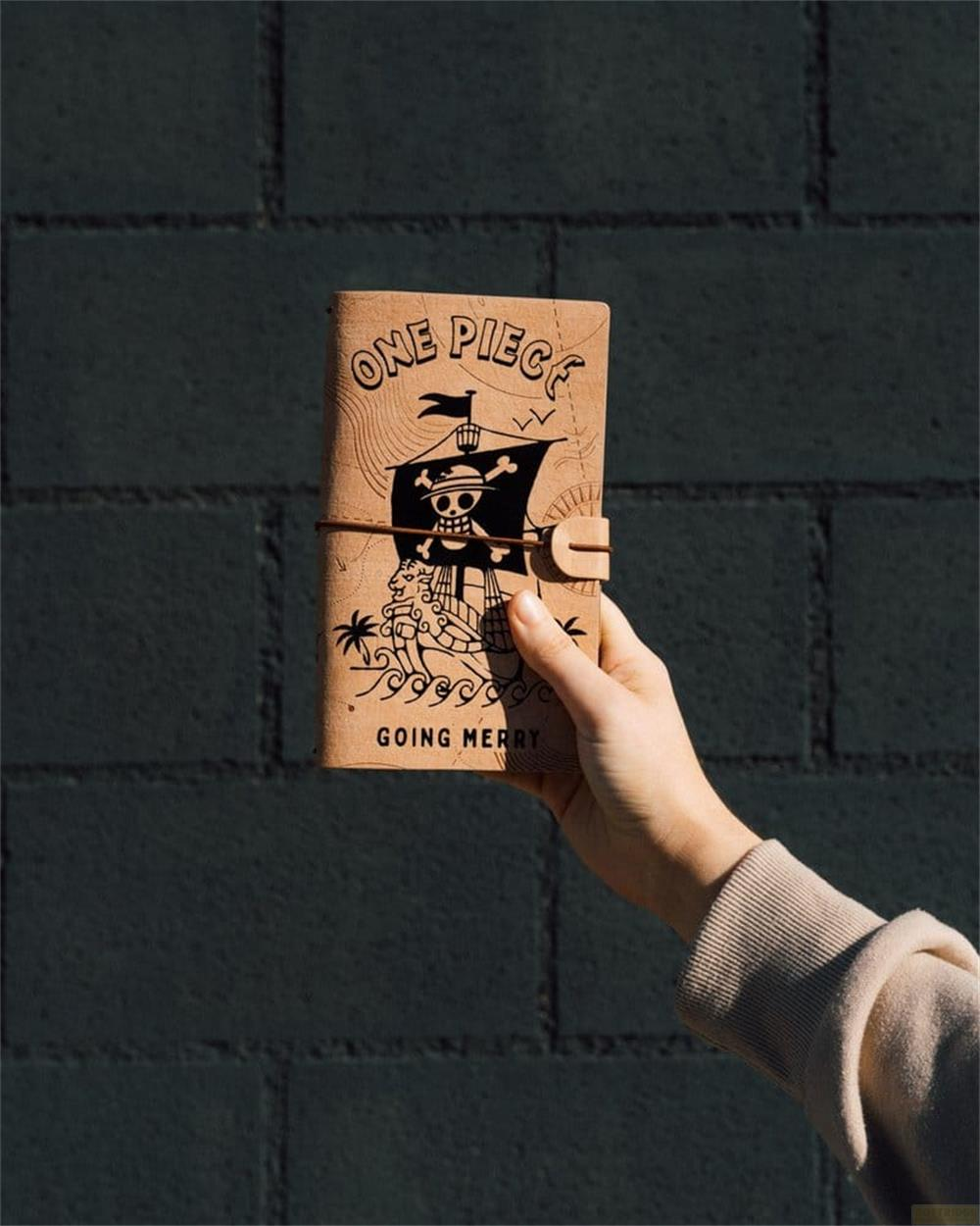 Eine Hand hält ein Notizbuch mit einem Piratenschiff und Totenkopf-Logo.