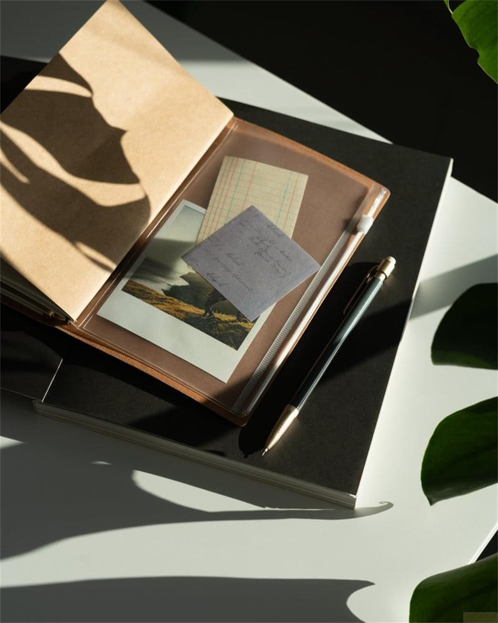 Offenes Notizbuch mit Foto, Notizen und Stift auf einem Tisch im Schatten.