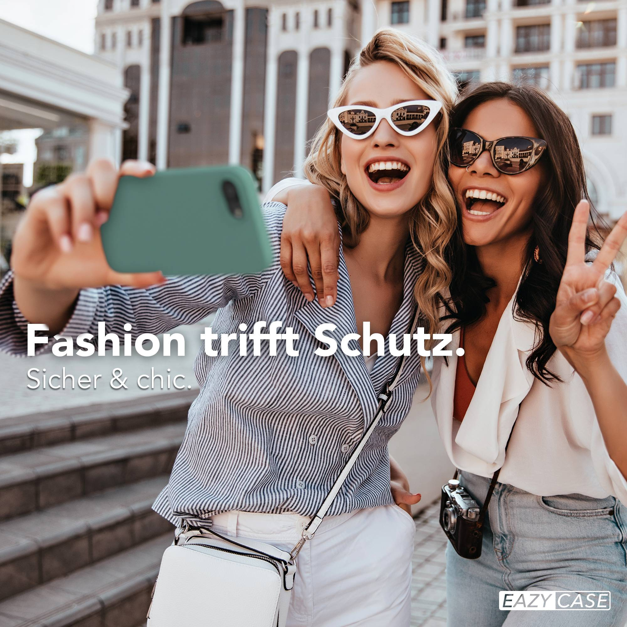 Zwei Frauen machen ein Selfie vor einem Gebäude, eine hält ein grünes Handy.