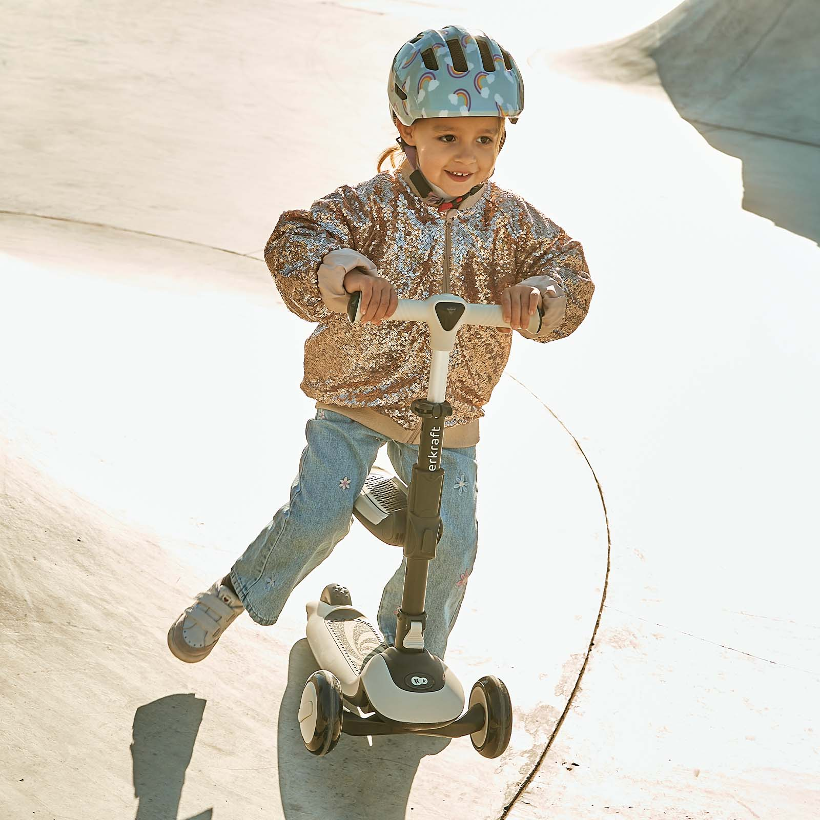 Ein Mädchen mit Helm fährt einen Roller auf einer Betonrampe.