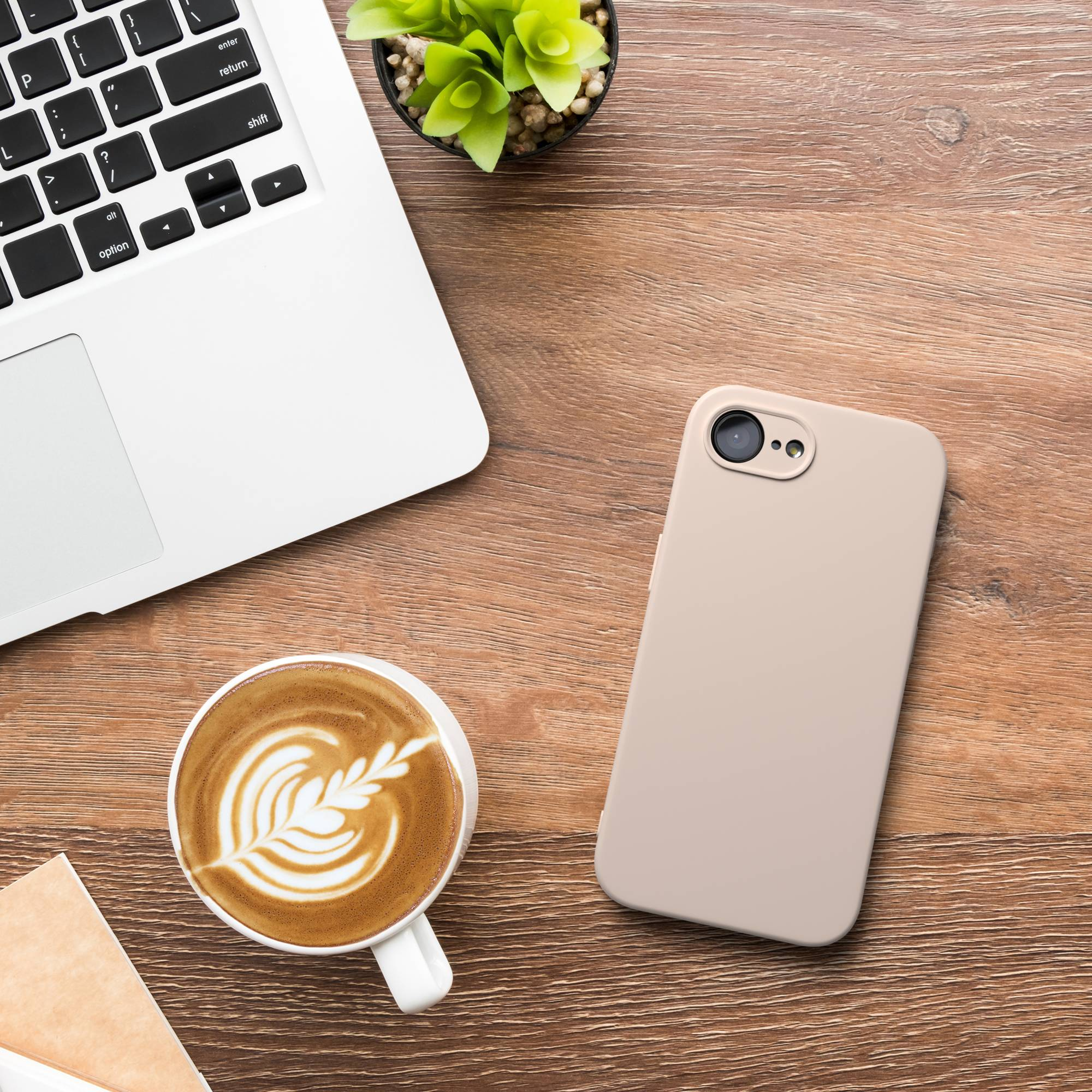 Ein Laptop, eine Kaffeetasse mit Latte Art und ein Handy liegen auf einem Holztisch.