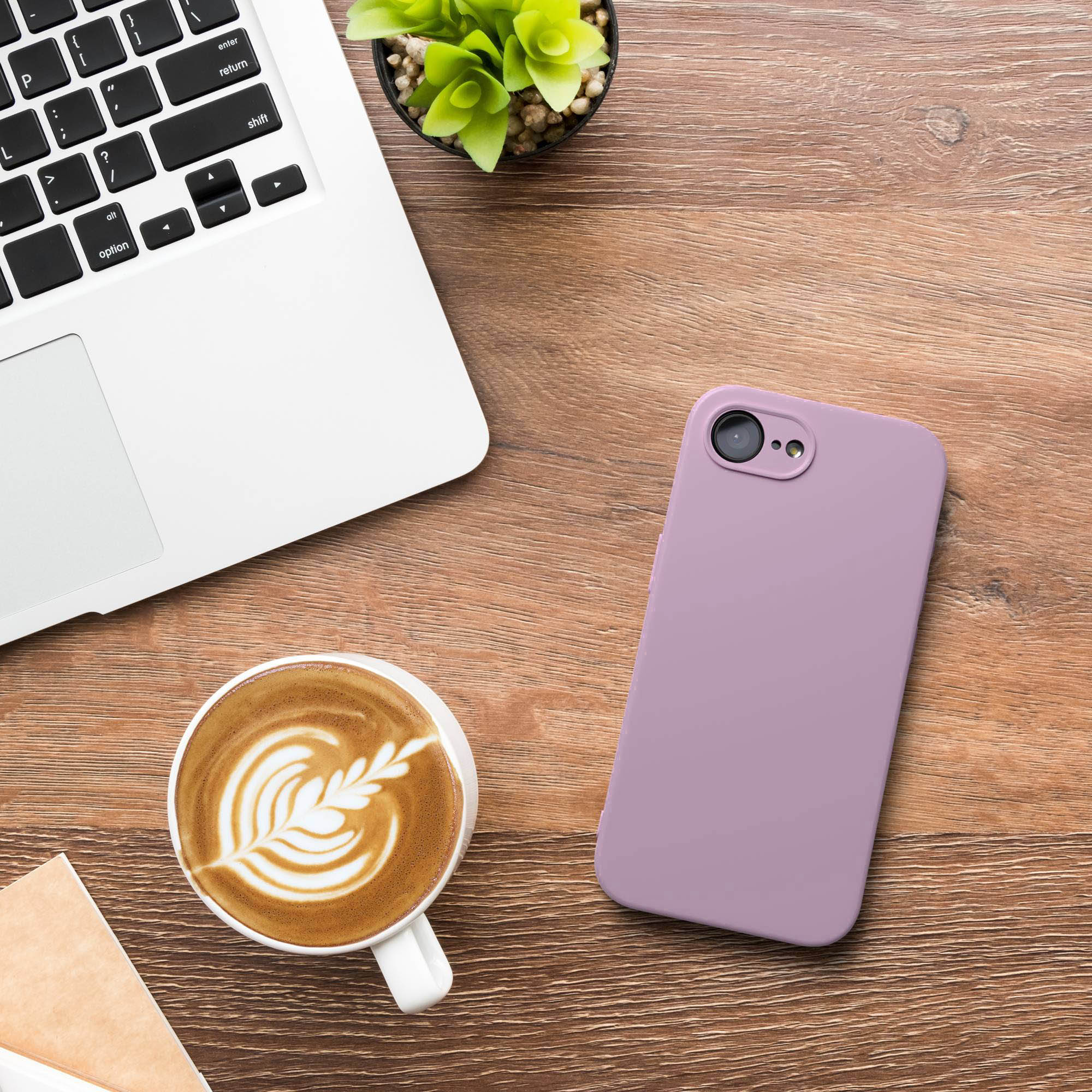 Eine Laptop-Tastatur, ein latte Art Kaffee und ein lila Handy auf einem Holztisch.
