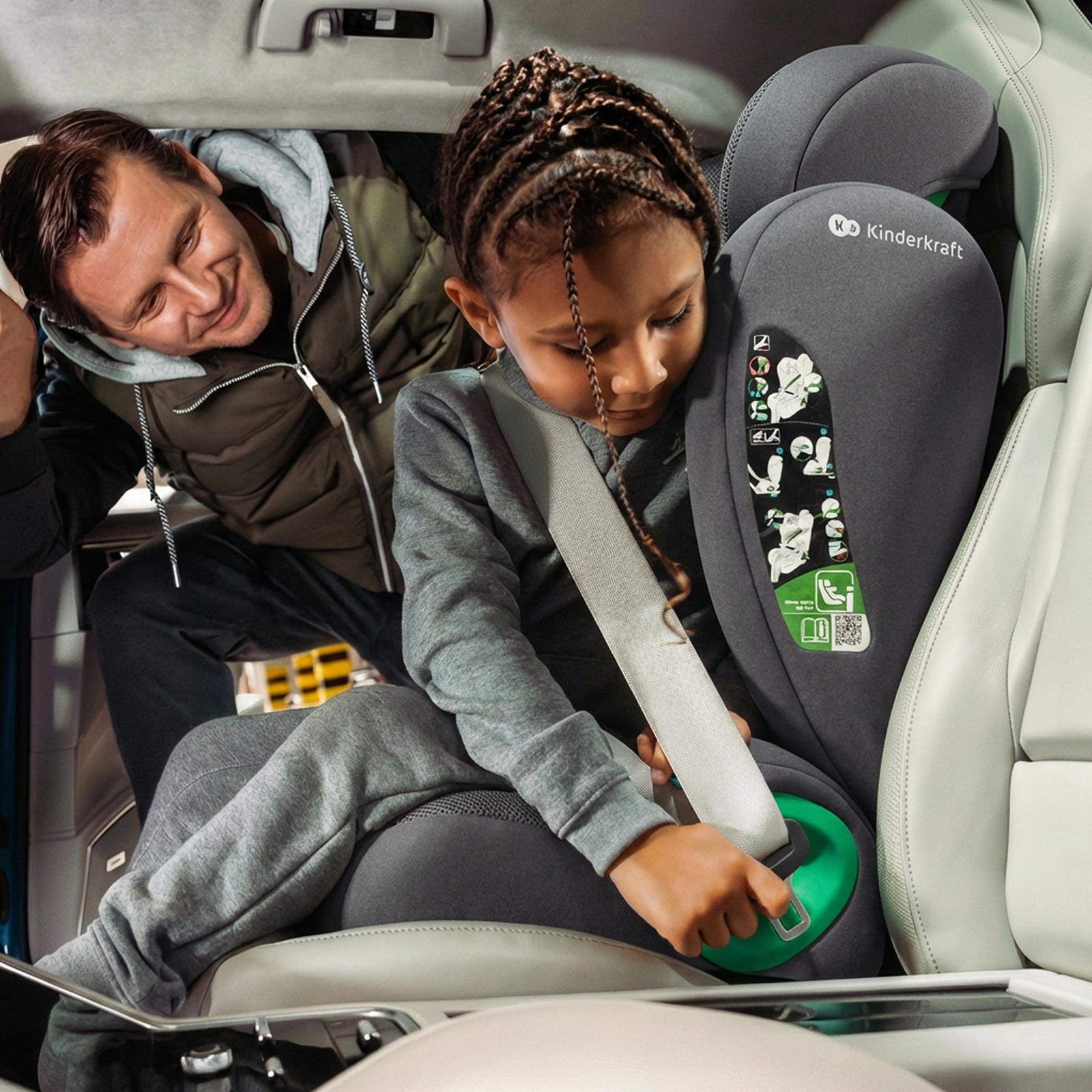 Vater hilft Tochter, Kindersitz mit grüner Schnalle im Auto zu sichern.