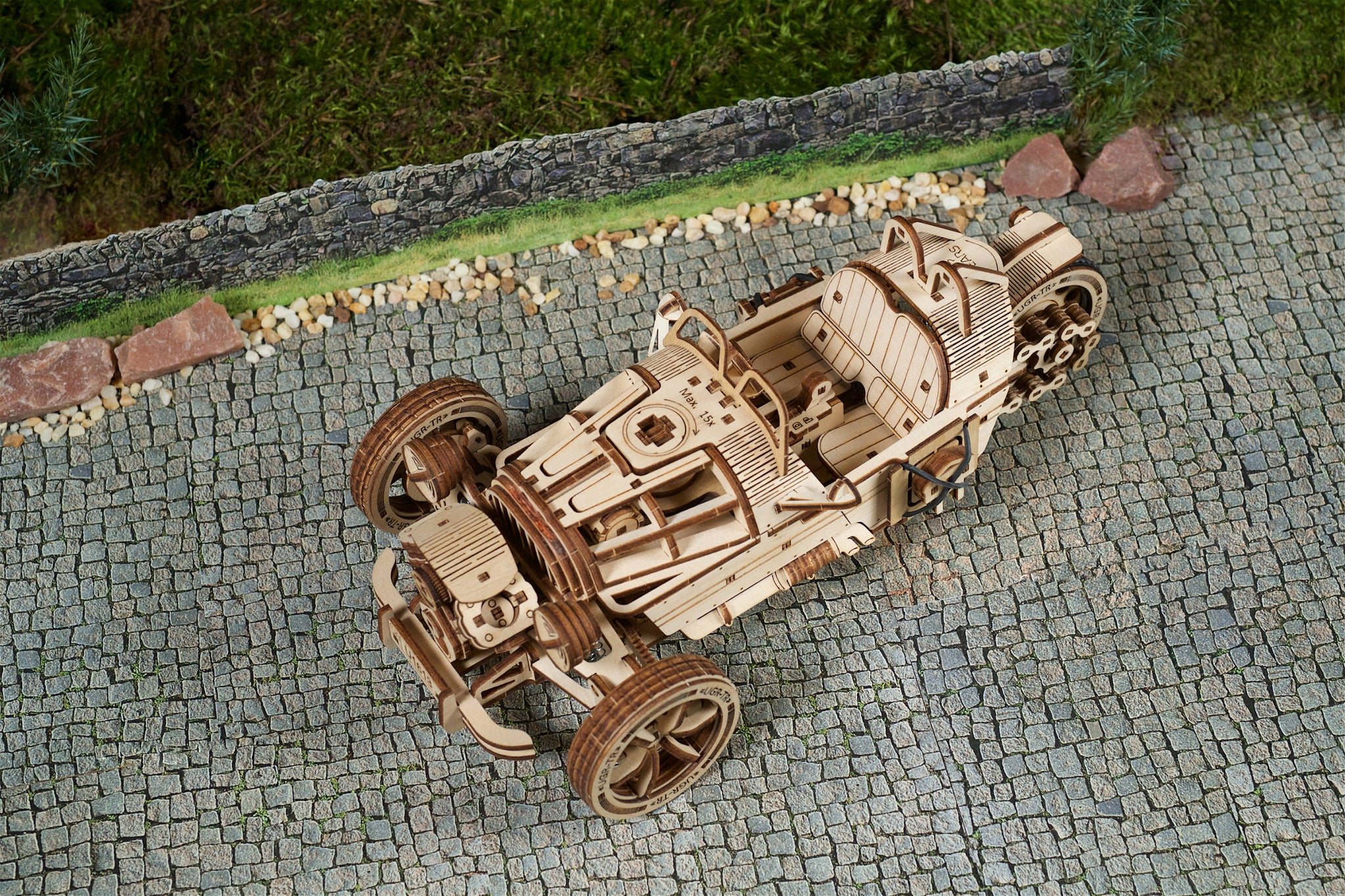 Modellino in legno di un'auto da corsa su ciottoli con muro di pietra e muschio.