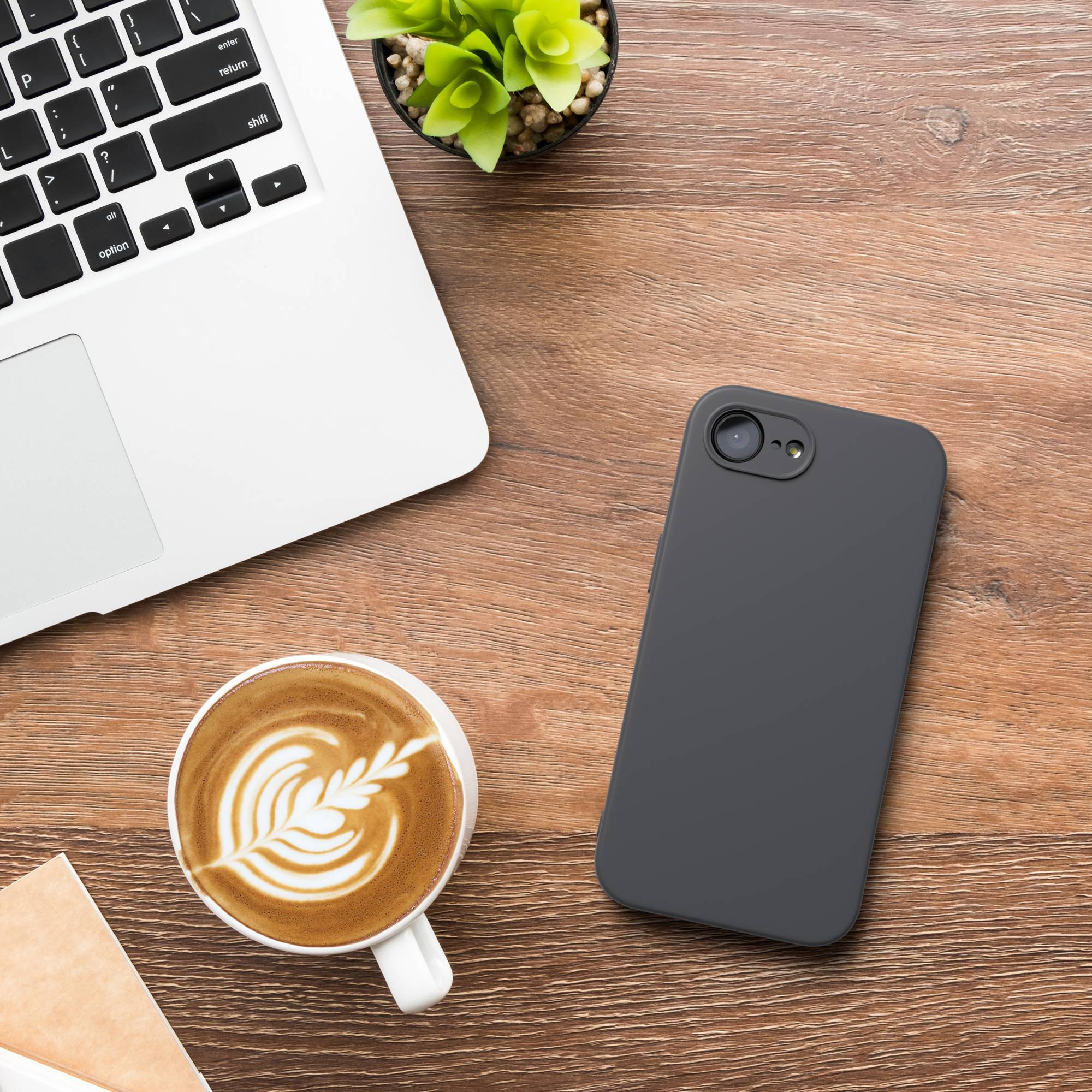 Ein Laptop, Kaffee mit Latte Art, ein Smartphone und eine Pflanze auf Holz.