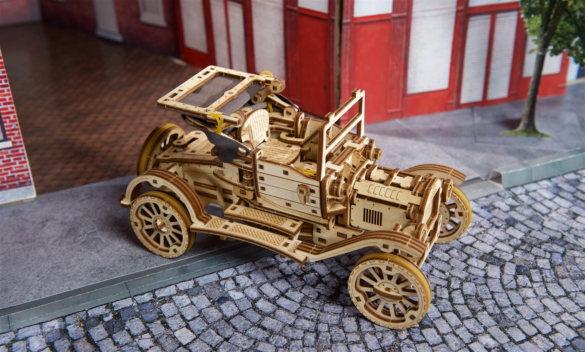 Ein hölzernes Modellauto im Vintage-Stil auf einer Kopfsteinpflasterstraße.
