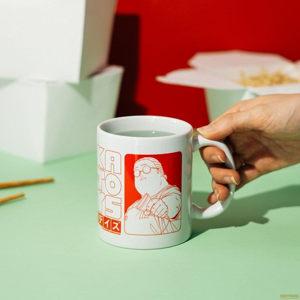 Una mano sostiene una taza blanca con un gráfico rojo. Una caja de comida está al fondo.