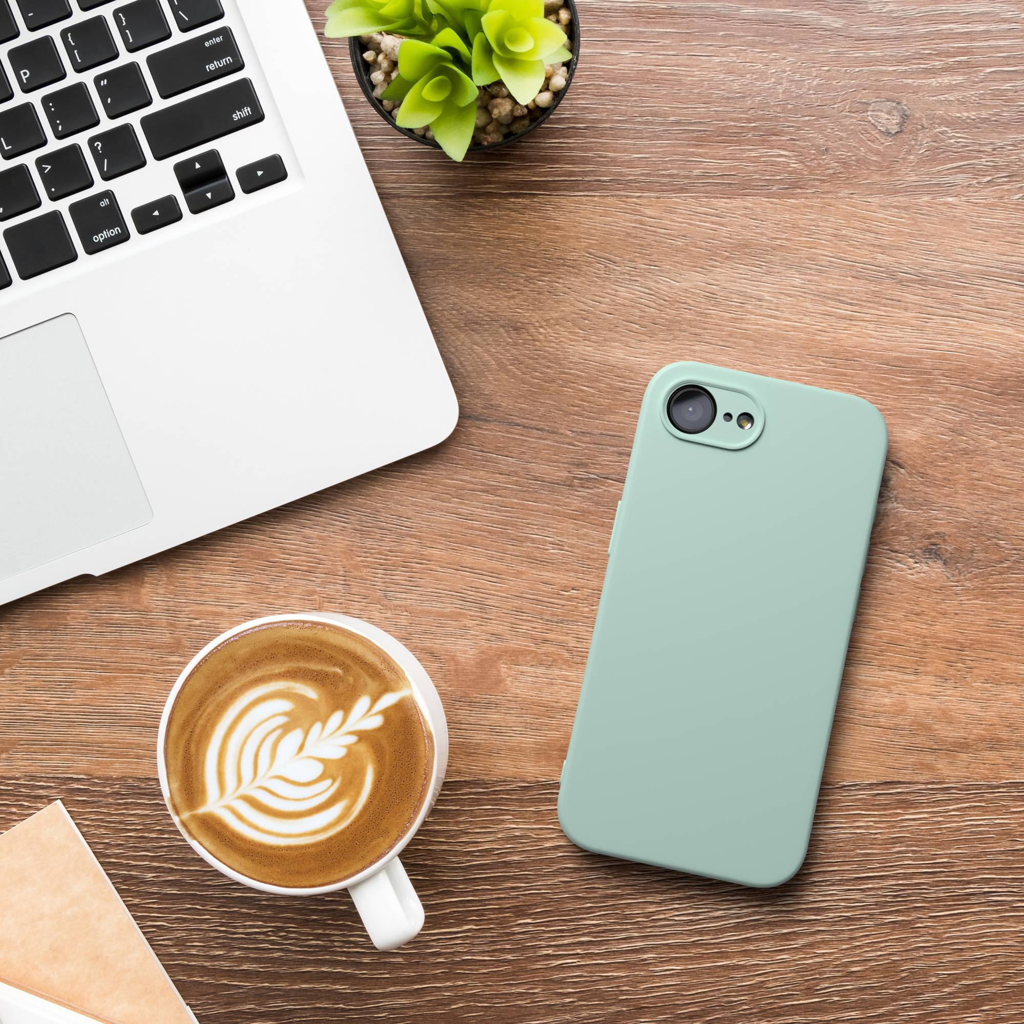 Ein Laptop, eine Kaffeetasse mit Latte Art und ein Handy auf einem Holztisch.
