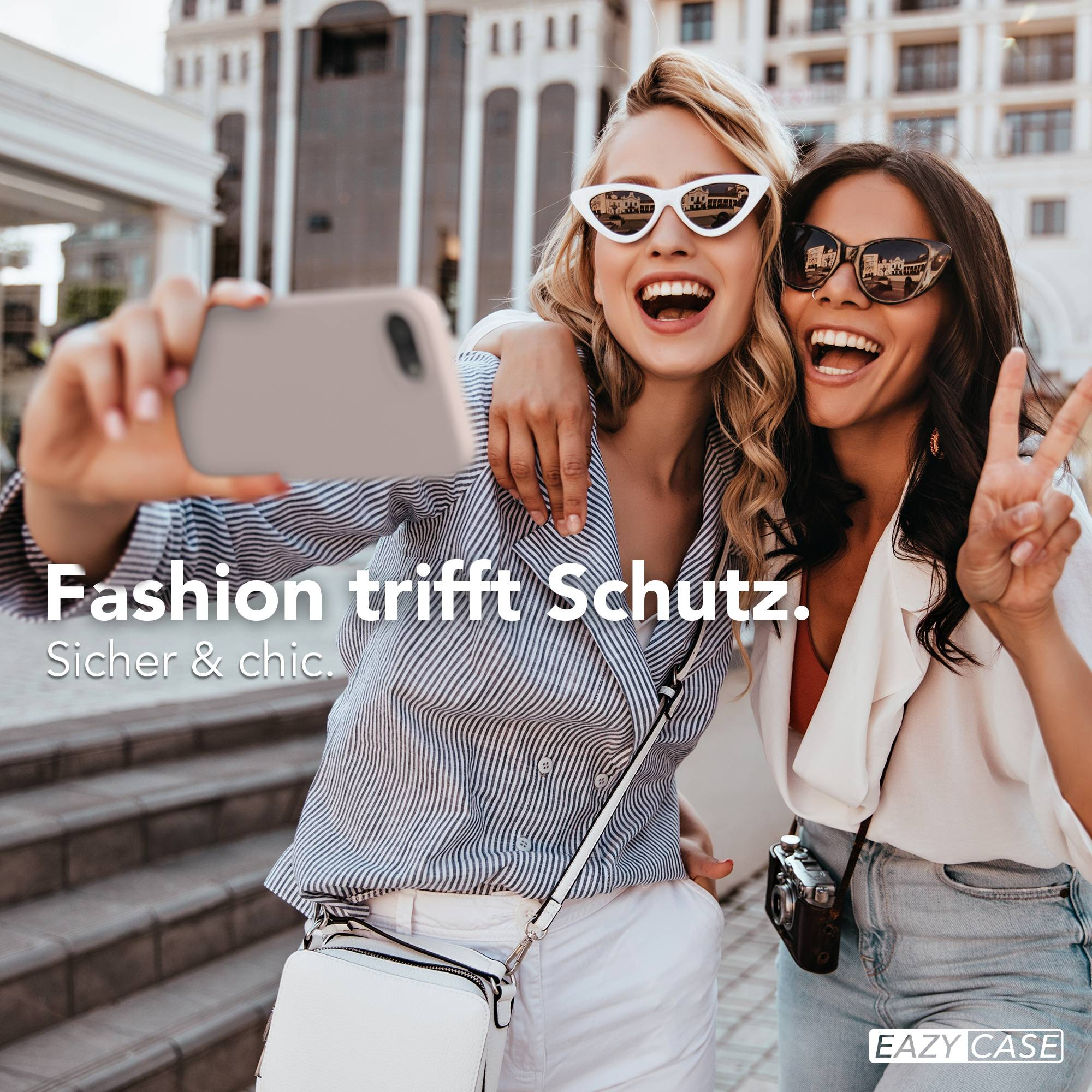 Zwei lachende Frauen machen ein Selfie vor einem Gebäude.
