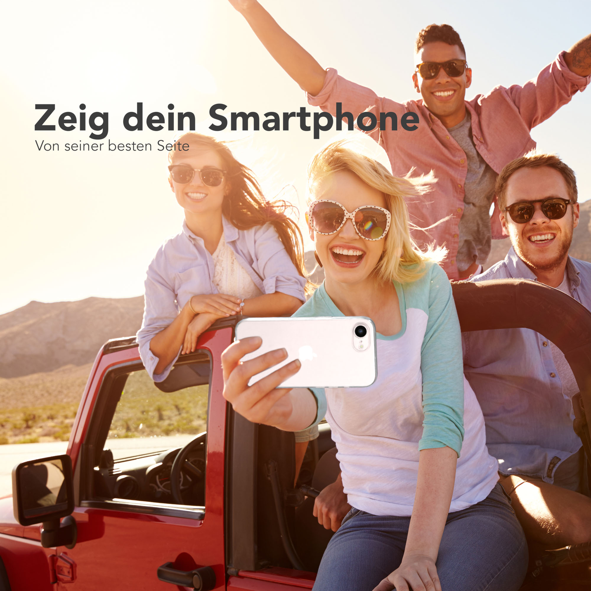 Vier Freunde im roten Jeep machen ein Selfie in der Wüste bei Sonnenschein.