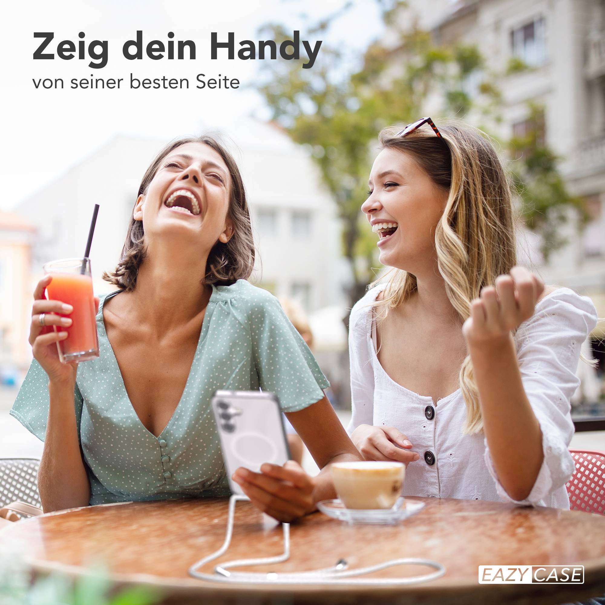 Zwei lachende Frauen sitzen an einem Tisch mit Getränken und einem Handy.