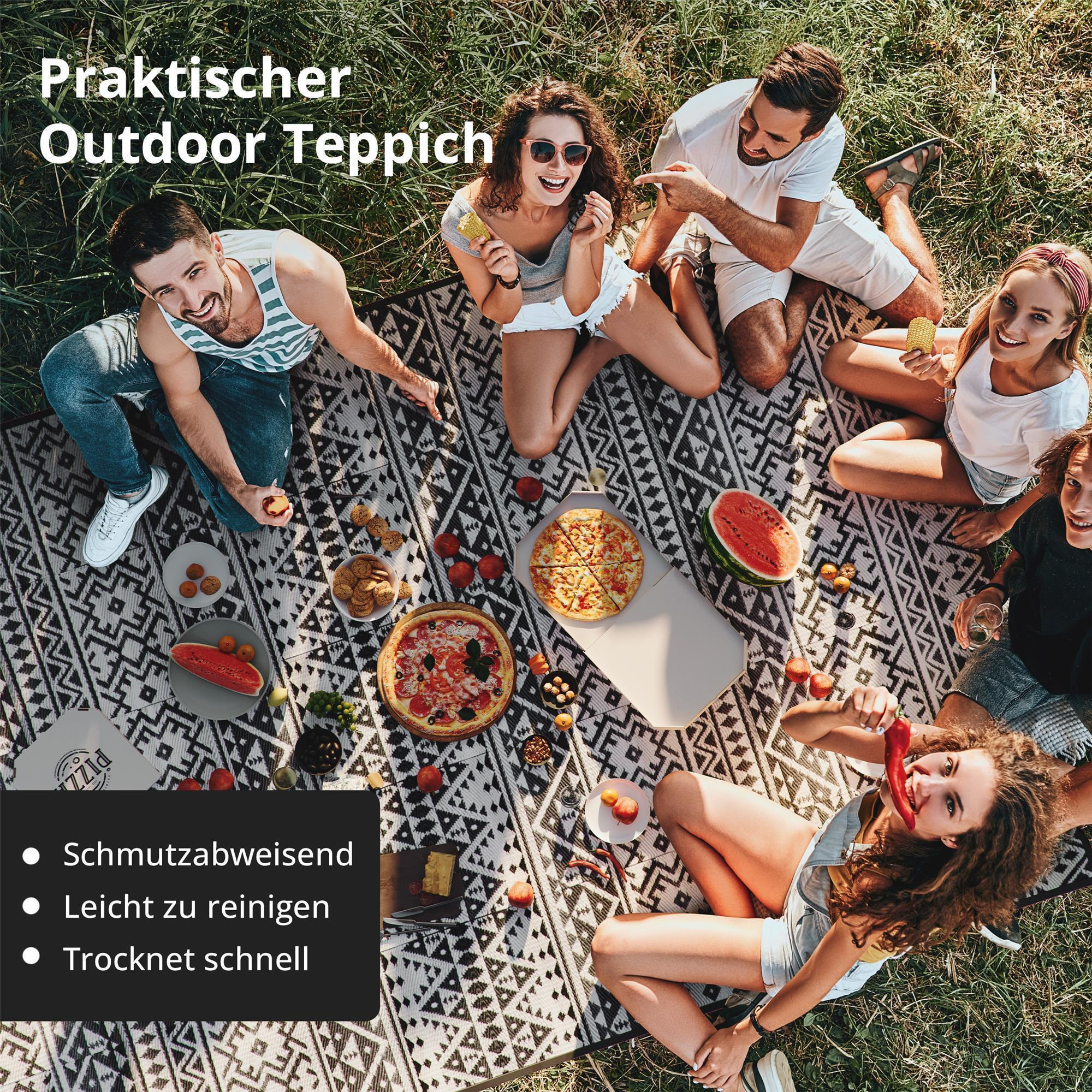 Freunde genießen ein Picknick im Freien mit Pizza, Wassermelone und Keksen auf einer Decke.