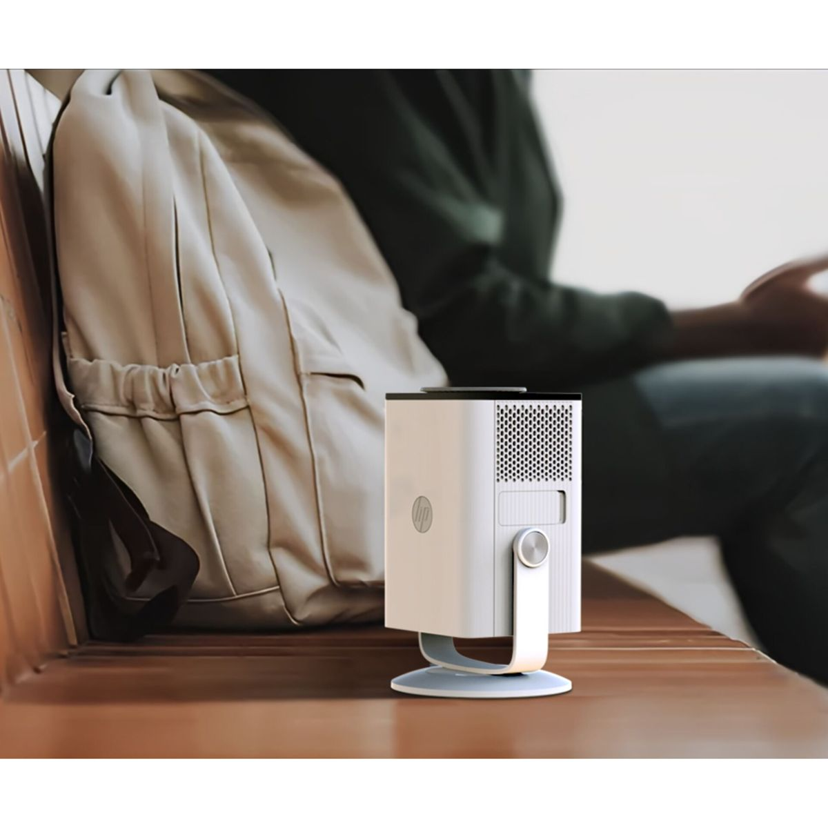 Ein weißer HP-Projektor steht auf einer Holzbank neben einem beige Rucksack.