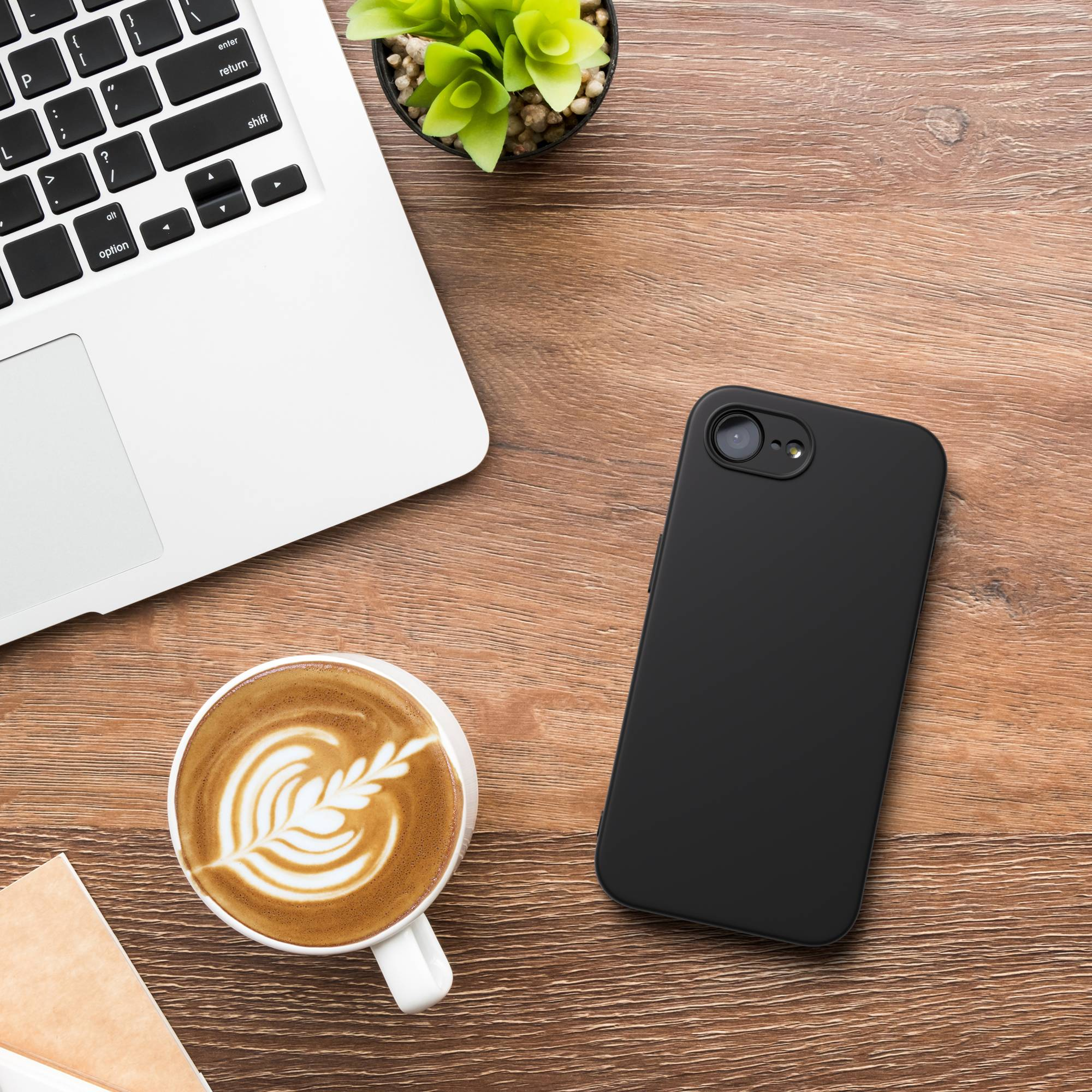 Ein Laptop, eine schwarze Handyhülle, ein Kaffee und eine Pflanze auf einem Holztisch.