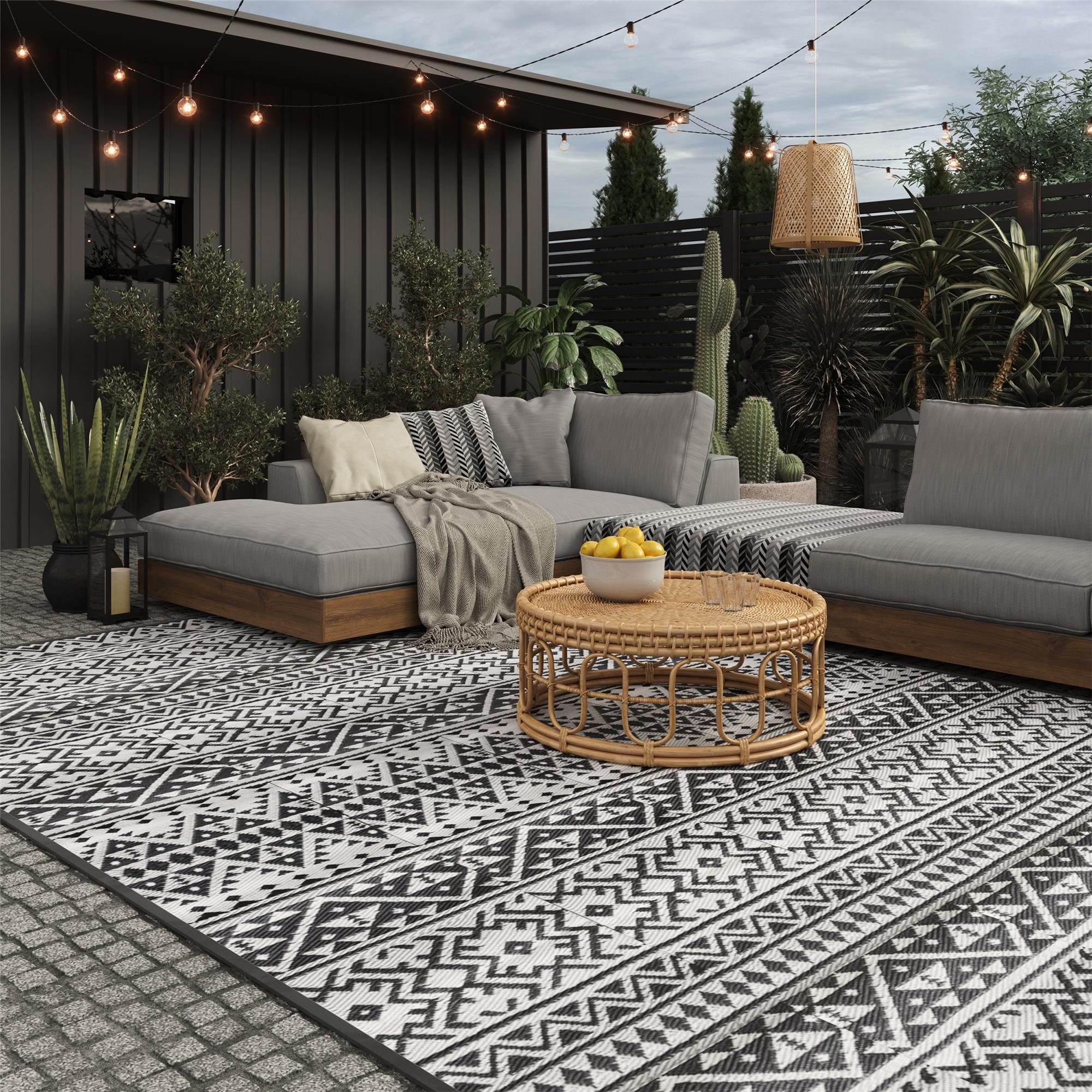 Graue Outdoor-Lounge mit Rattantisch, Zitronen und Lichterkette.