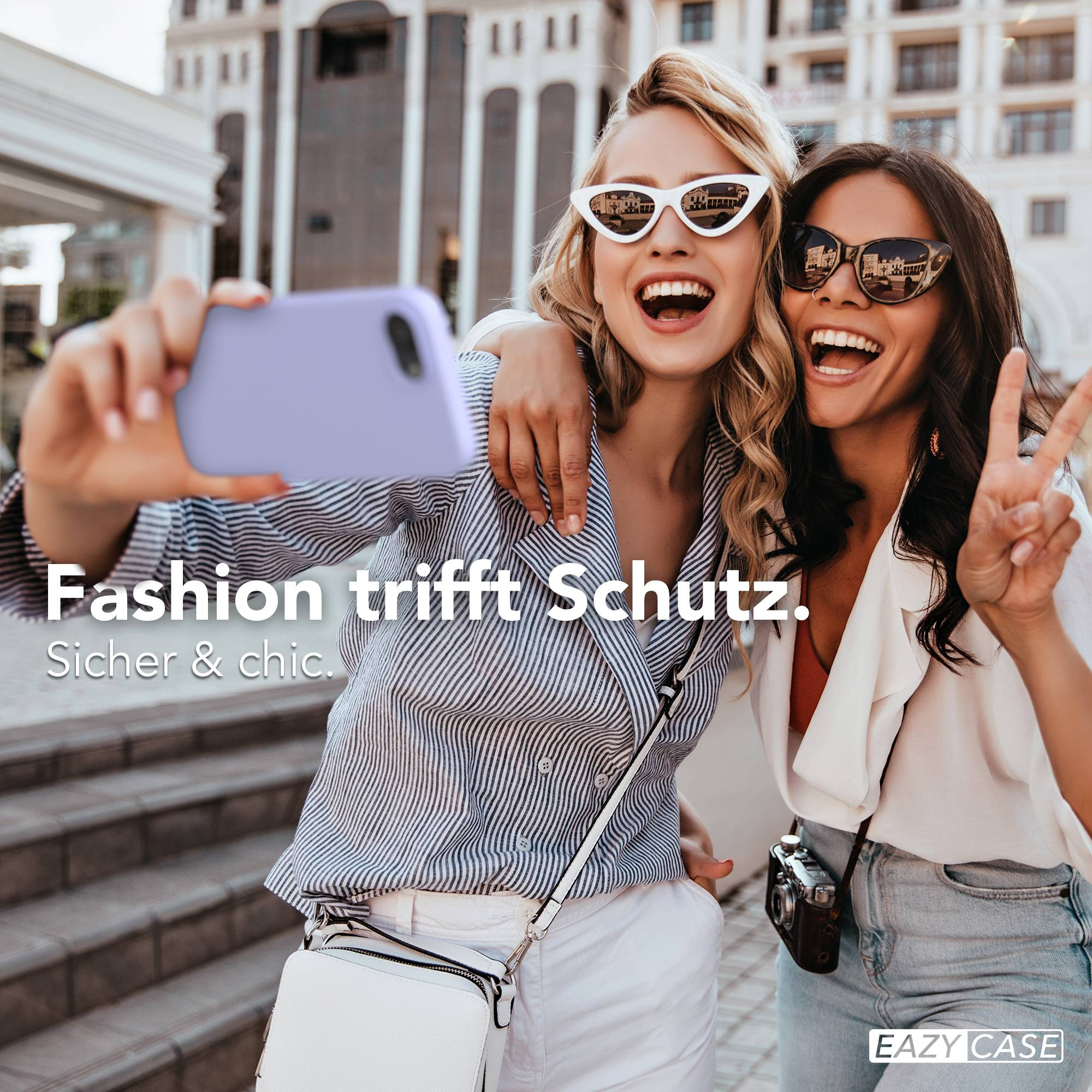 Zwei lachende Frauen machen ein Selfie mit einem lila Handy vor einem Gebäude.