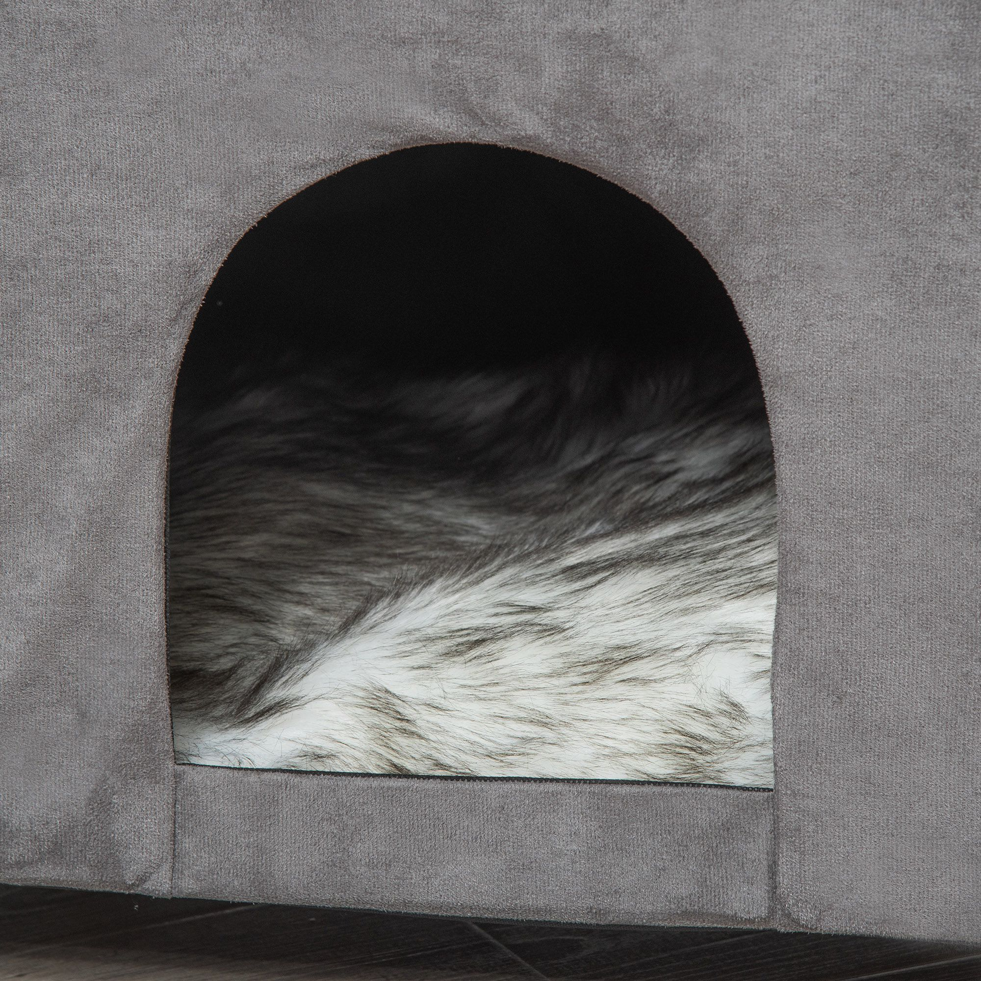 Cama gris para mascotas con forro mullido blanco y gris y una entrada oscura.