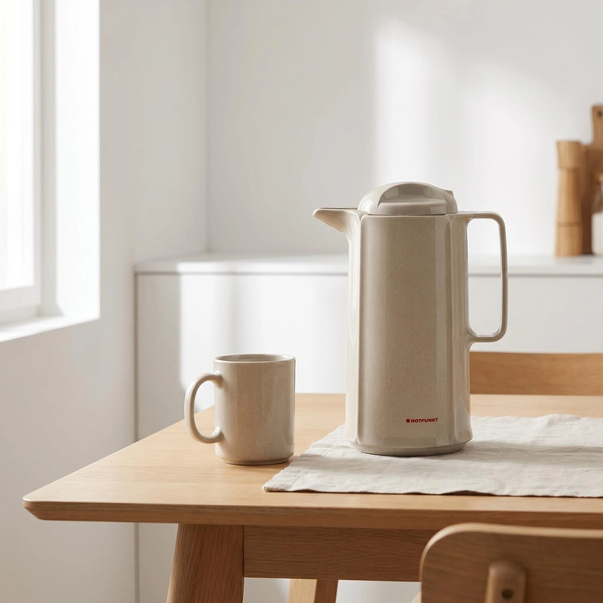 Eine beige Thermoskanne und eine Tasse stehen auf einem Holztisch.