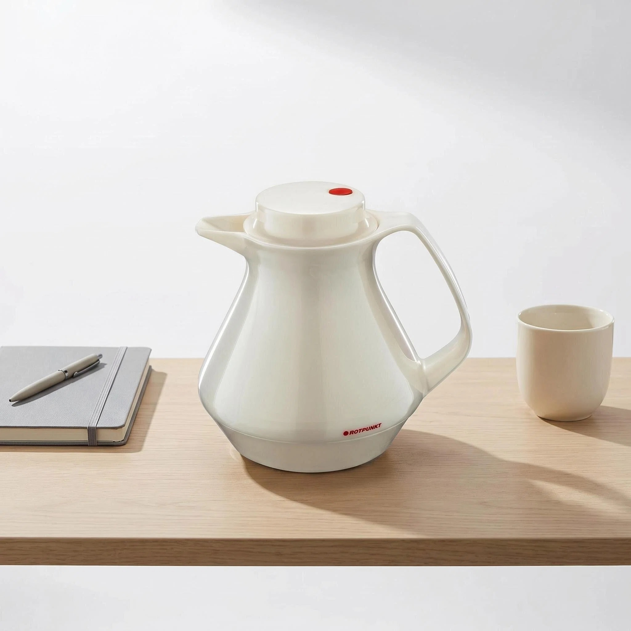 Ein weier Thermoskanne mit rotem Punkt, daneben ein Notizbuch und eine Tasse.