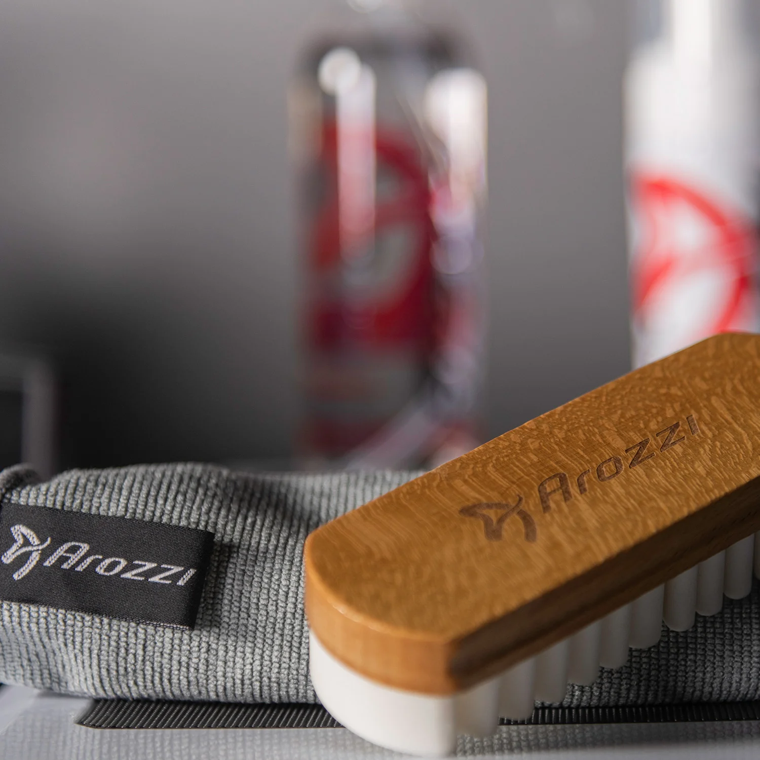A grey microfiber cloth with Arozzi logo rests beside a wooden brush with white bristles.