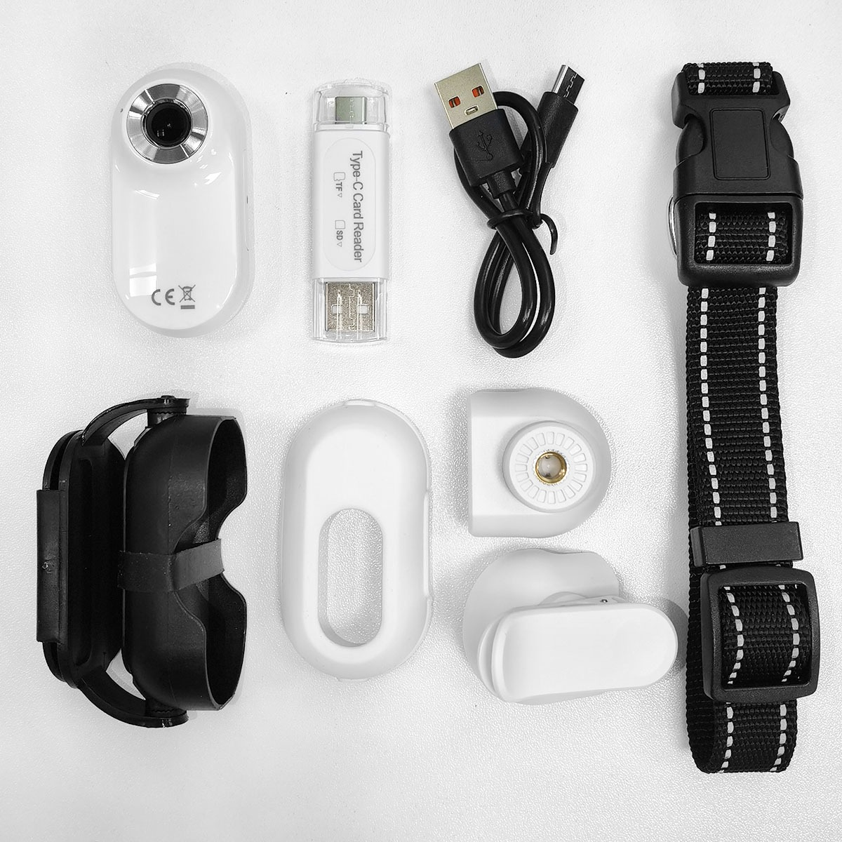 Cámara blanca, lector de tarjetas, cable USB, correa negra, soportes blancos.