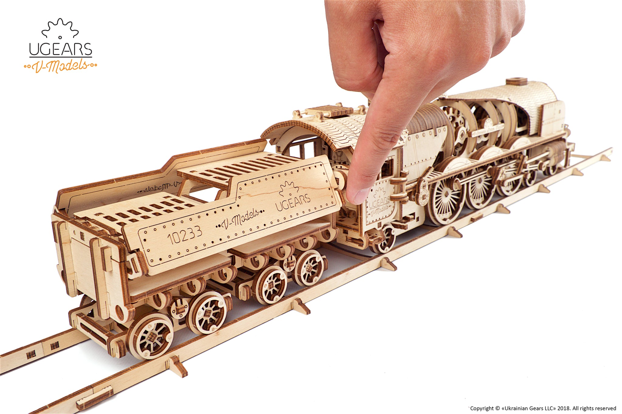 Ein Finger berührt ein Holzmodell einer Dampflokomotive auf Gleisen.