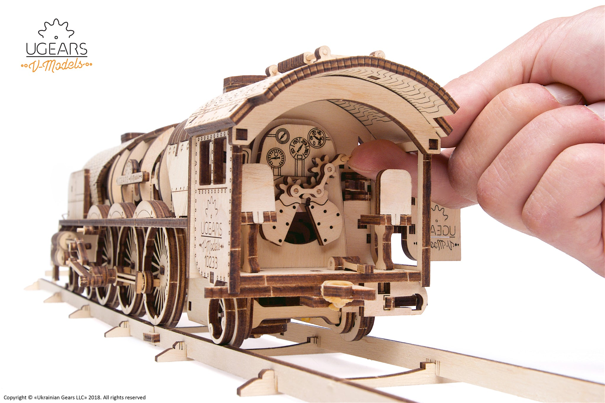 Ein Mann berührt ein Holzmodell einer Lokomotive mit Zahnrädern und Zifferblättern.