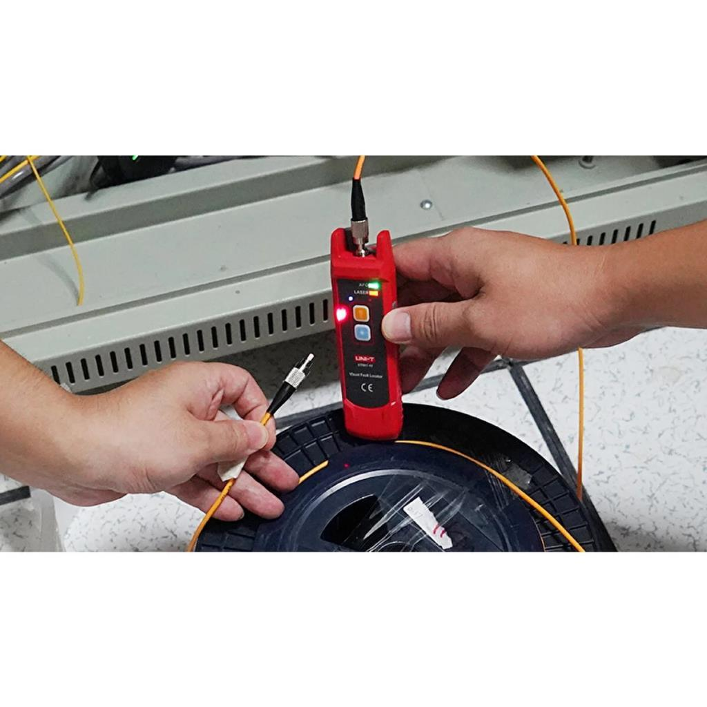 Eller kırmızı fiber optik arıza bulucu ve sarı kablo tutuyor.